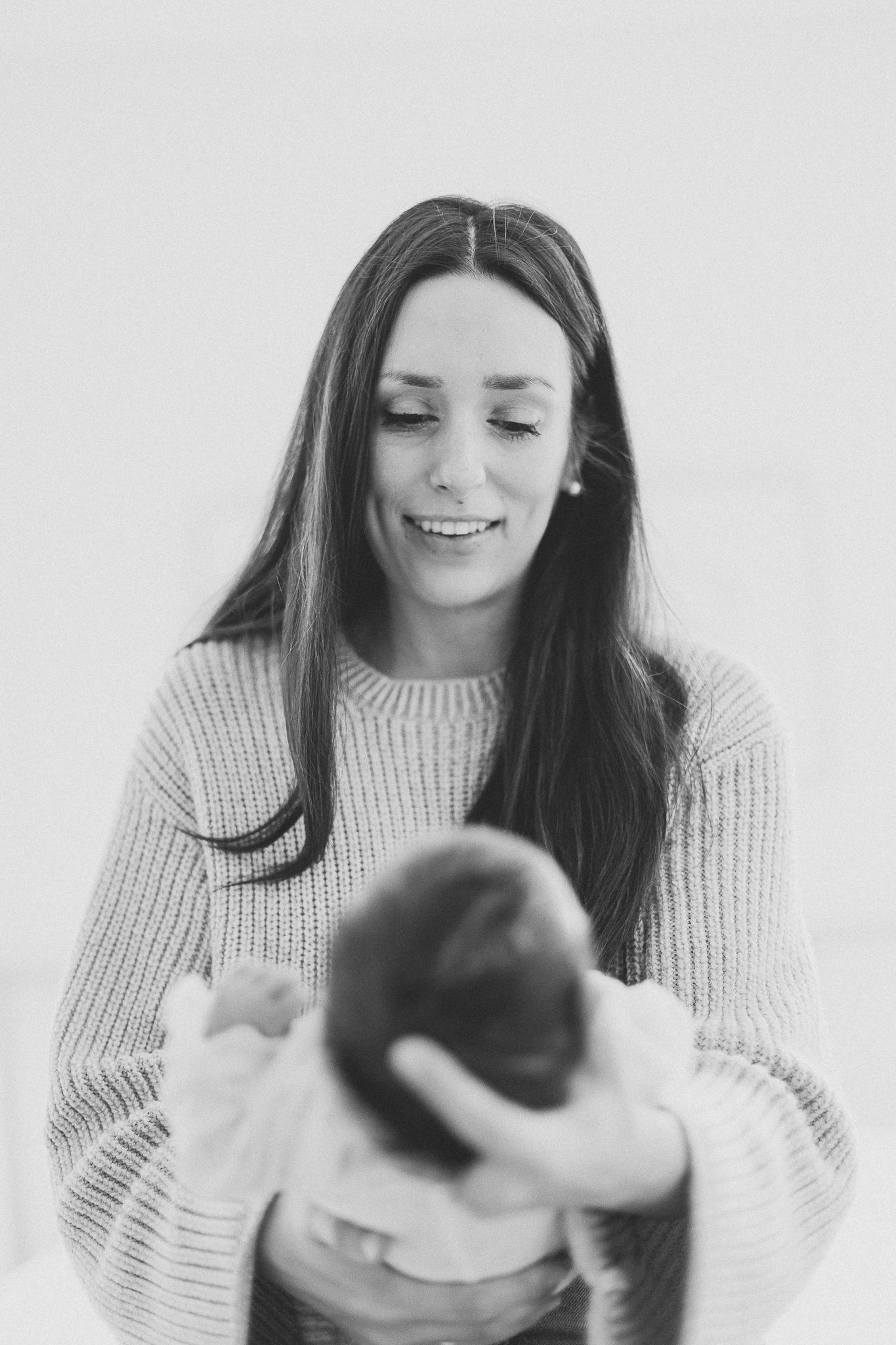 Parent en pull blanc tenant son nouveau-né, série noir et blanc capturée pour moments tendres et atmosphère chaleureuse et intime