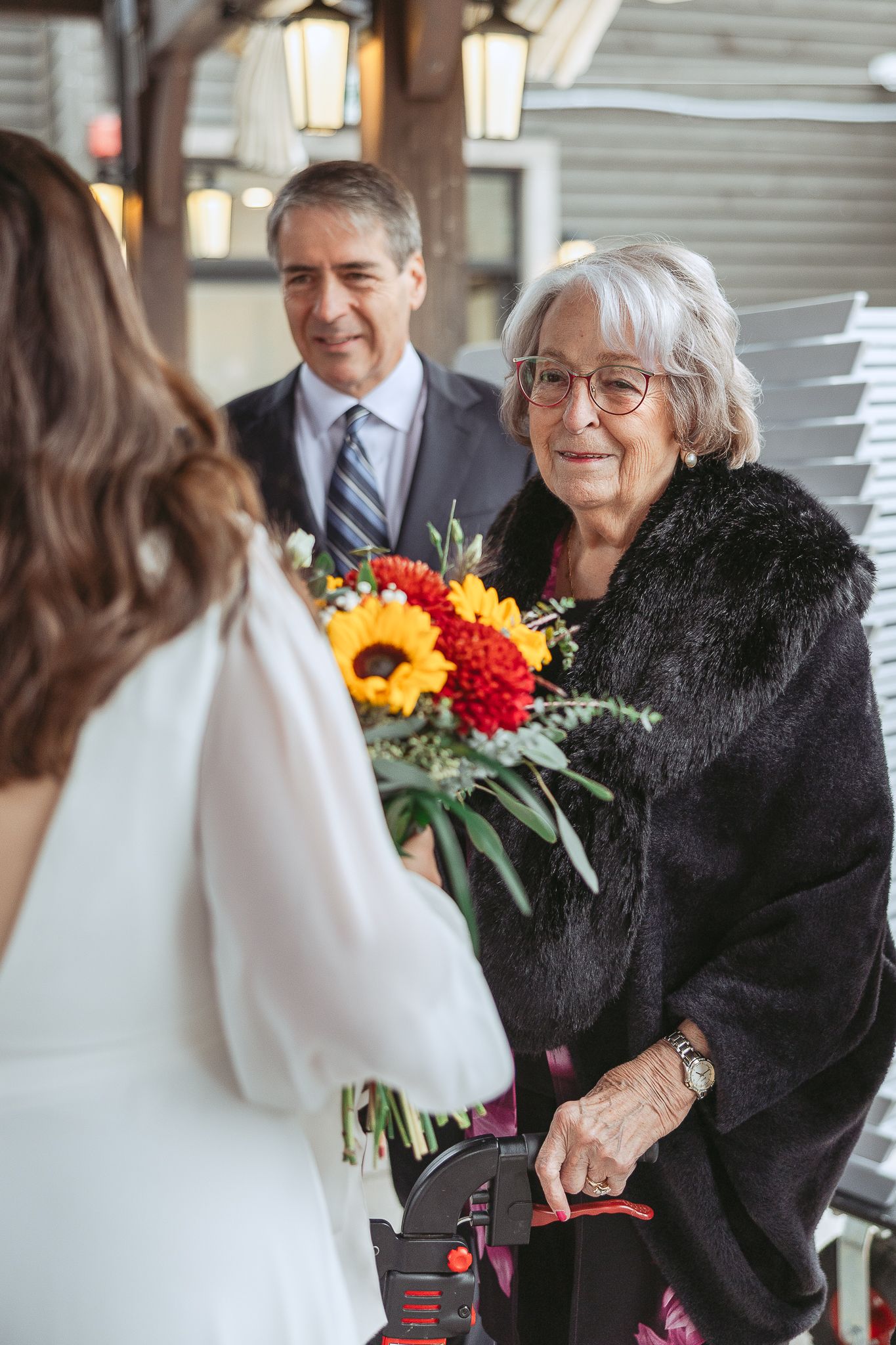 La grand-mère sourit devant sa petite fille à son mariage avec un bouquet coloré de tournesols et de fleurs rouges