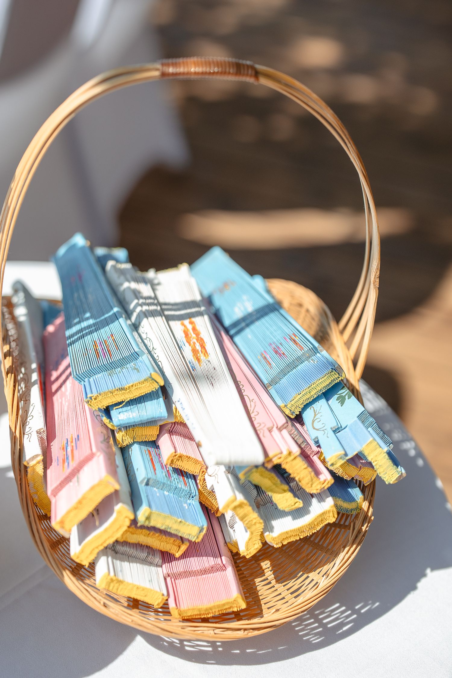 Panier tressé rempli de cadeaux invités colorés aux tons rose et bleu, éclairé par une lumière naturelle lors du mariage.