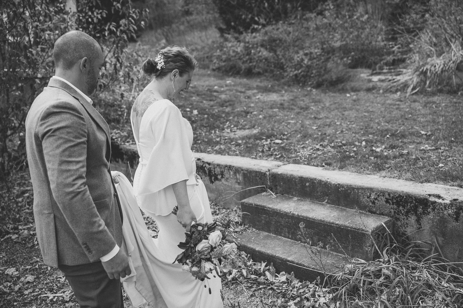 Noir et blanc Moment romantique de mariage en extérieur à l’automne, avec feuillage coloré et maisons en arrière-plan.