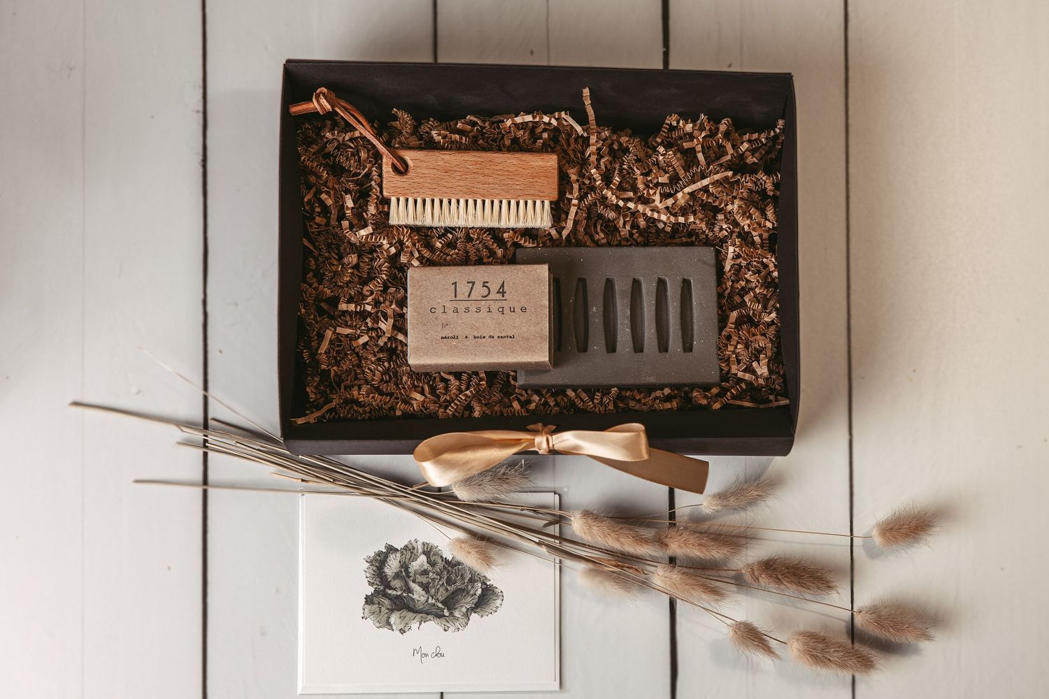 Coffre-cadeau présenté dans un décor minimaliste avec boîtes décoratives et éléments botaniques séchés aux tons neutres