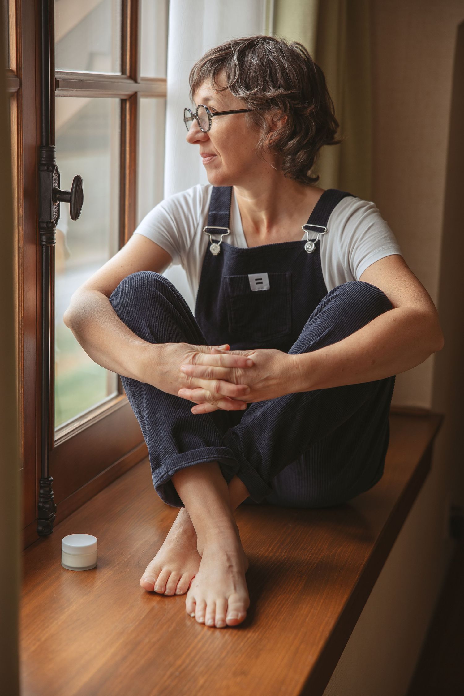 Person sitting by window with bare feet on wooden surface.