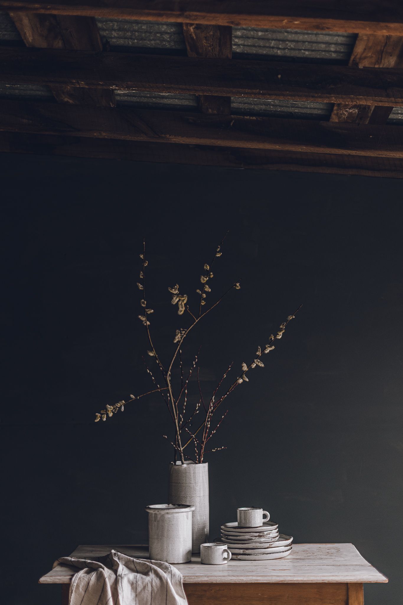 Table minimaliste avec vaisselle en céramique blanche et branches délicates dans un vase, photographiée sur fond sombre
