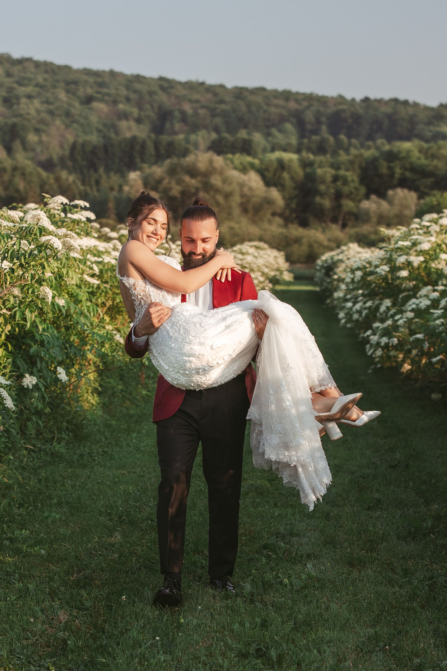 Couple de mariés posant avec légèreté dans un champ de fleurs sauvages blanches à l’heure dorée, lors d’une séance photo en extérieur.