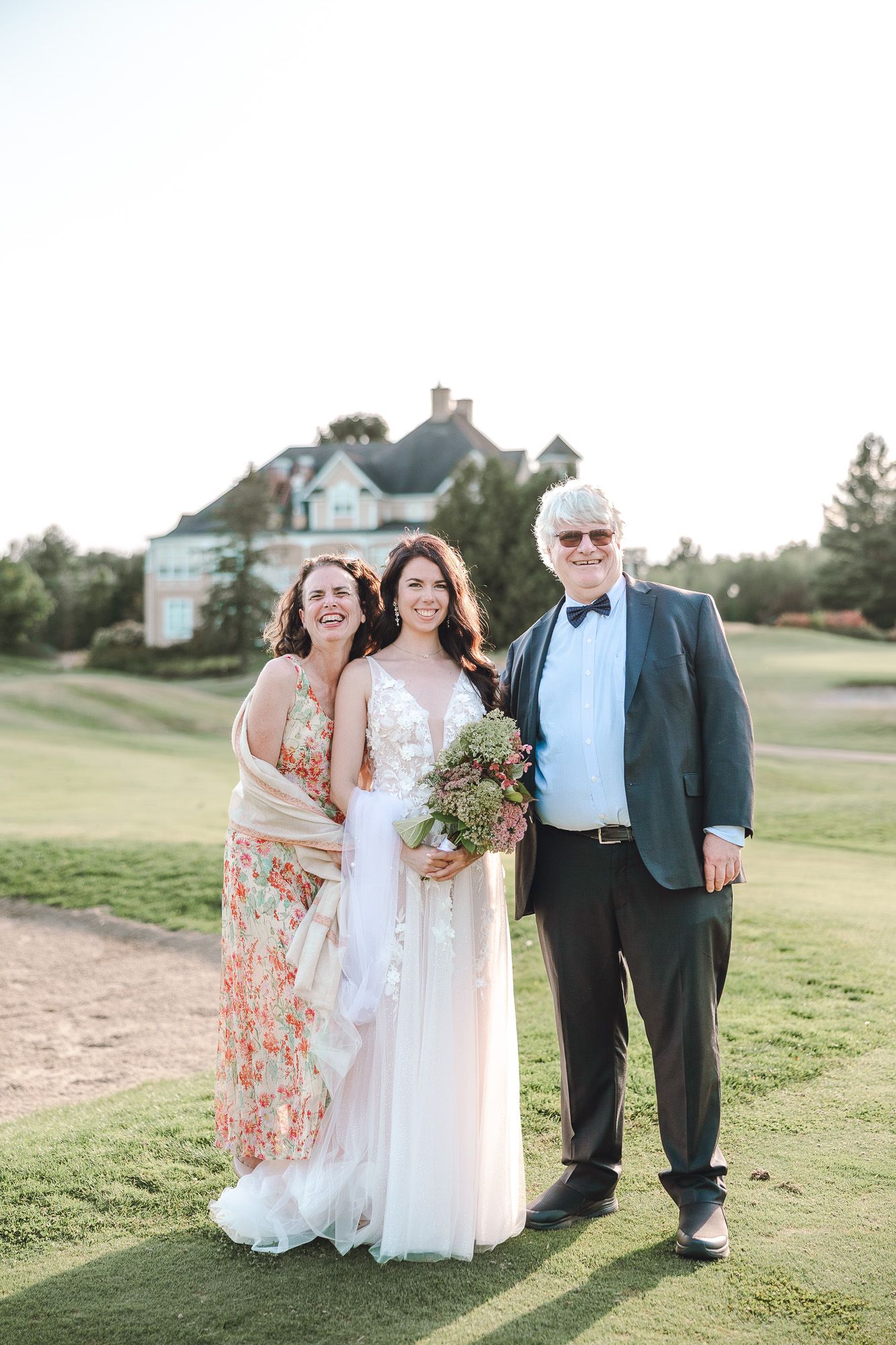 Cortège de mariage posant sur un terrain de golf ensoleillé, avec une maison élégante en arrière-plan