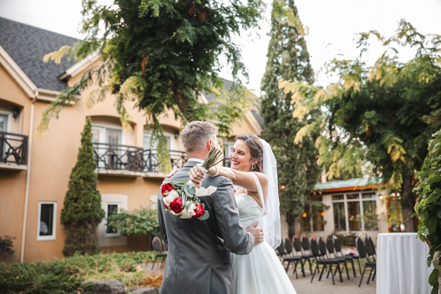 A romantic outdoor wedding moment at a venue with peach-colored buildings and lush greenery.