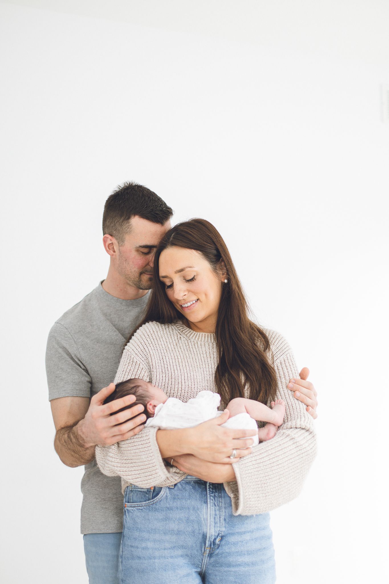 Nouveau-né dans les bras de ses parents devant mur blanc à domicile, capturé pour moments familiaux intimes et chaleureux