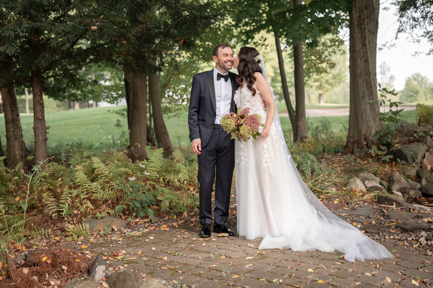 Couple en tenue de mariage debout ensemble dans un décor boisé aux couleurs d’automne, en Estrie