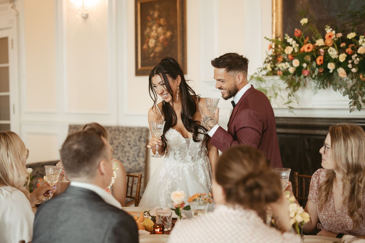 Wedding guests gather in an elegant ballroom decorated with floral arrangements and warm lighting for a celebration.