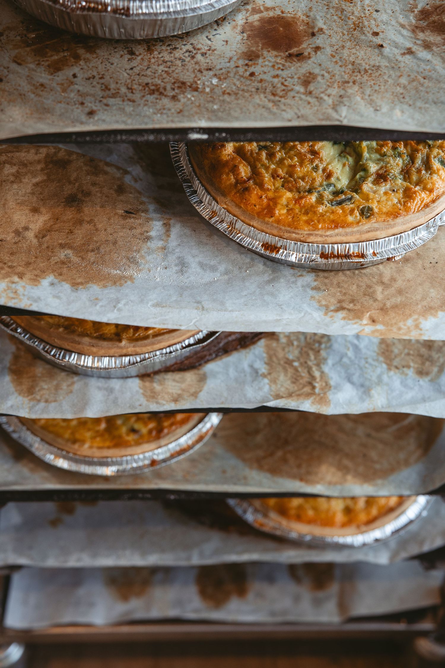 Close-up view of multiple savory pies in aluminum foil tins arranged on a rustic surface.