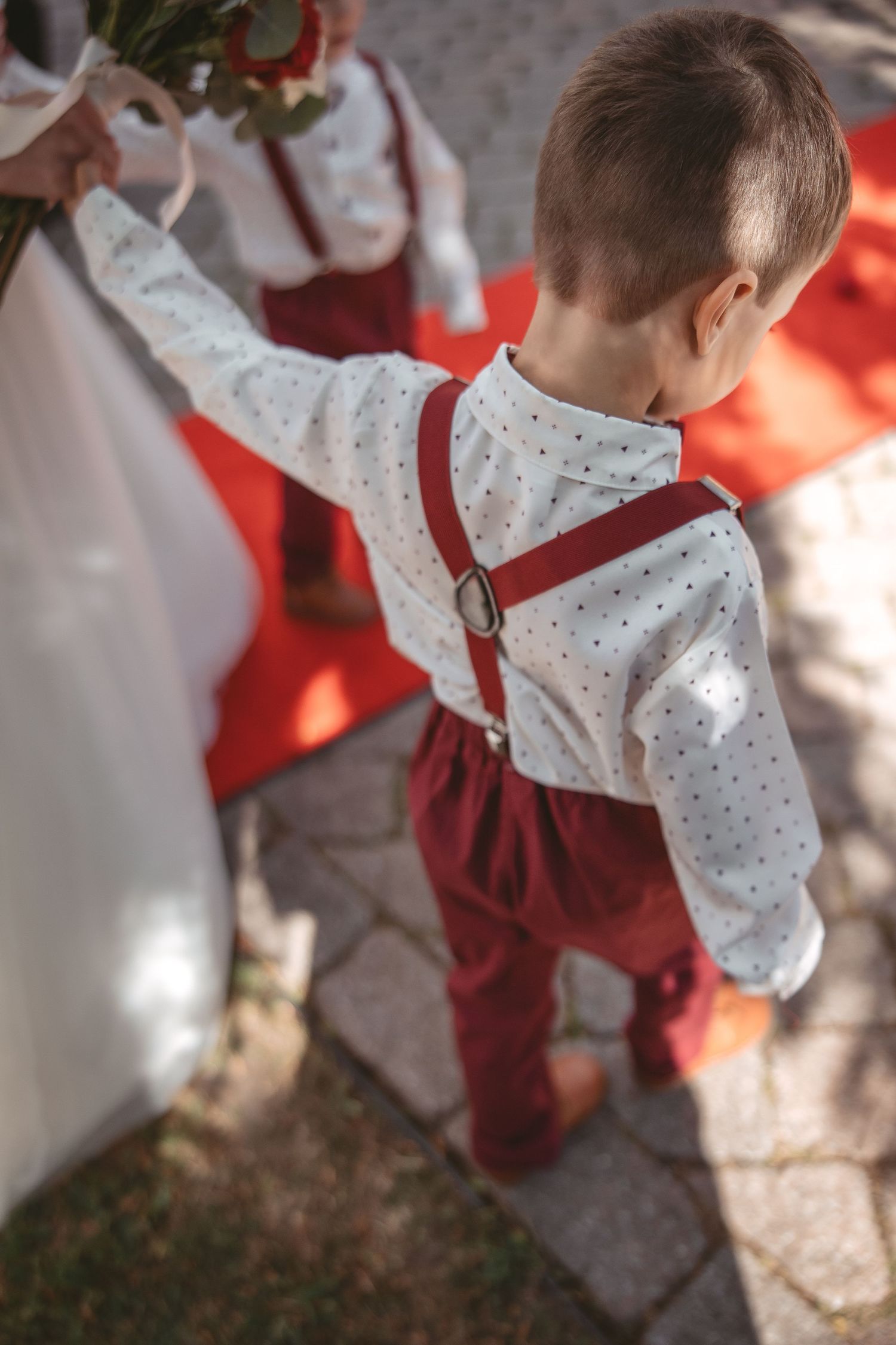 A child wearing a polka dot shirt and red suspenders stands outdoors in soft lighting.