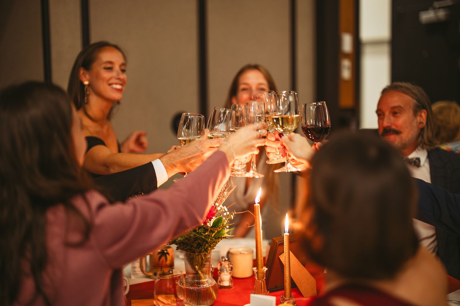 Des amis profitent de boissons et de conversations lors d’un mariage, avec des verres de vin et des bougies sur la table.