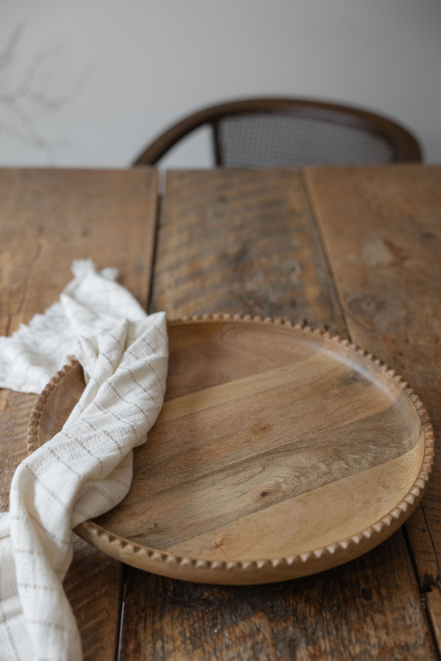 Rustic wooden serving board with beaded edge detail and white linen napkin on weathered table.