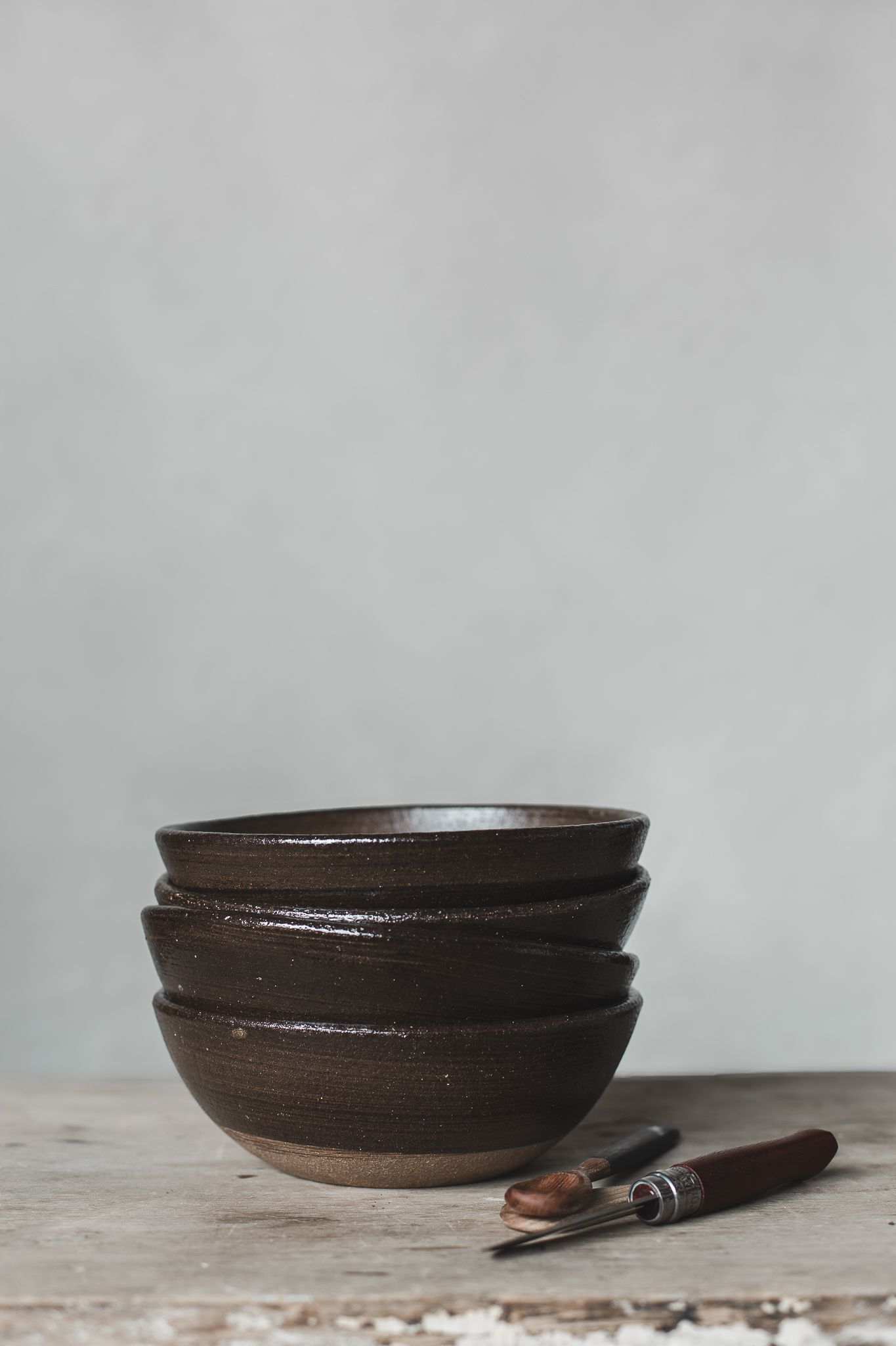 Empilement de bols en céramique brun foncé avec ustensile en bois sur table rustique, photographiés pour mettre le produit en valeur