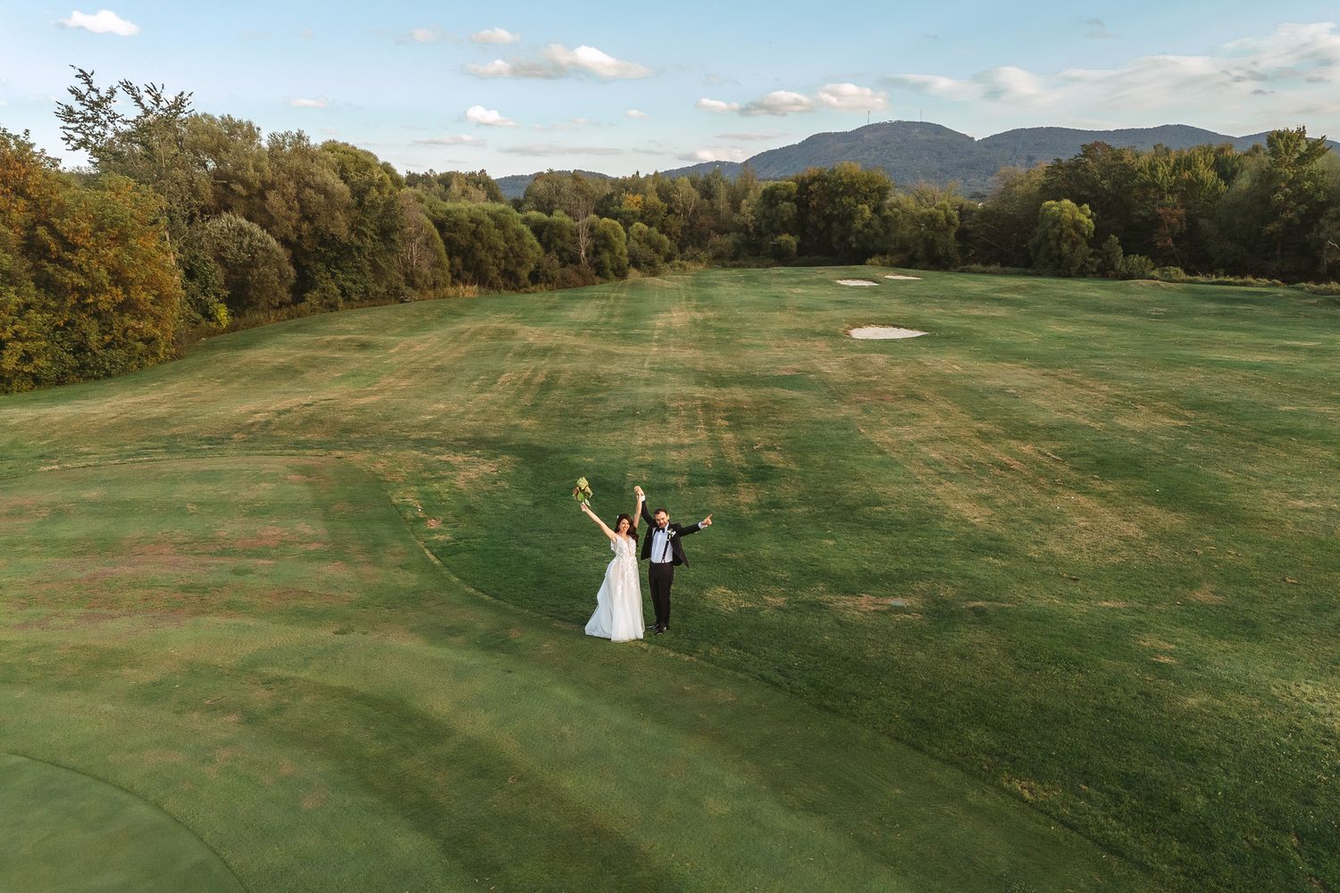 Vue aérienne d’un couple célébrant sur un terrain de golf pittoresque, avec montagnes et arbres d’automne en arrière-plan