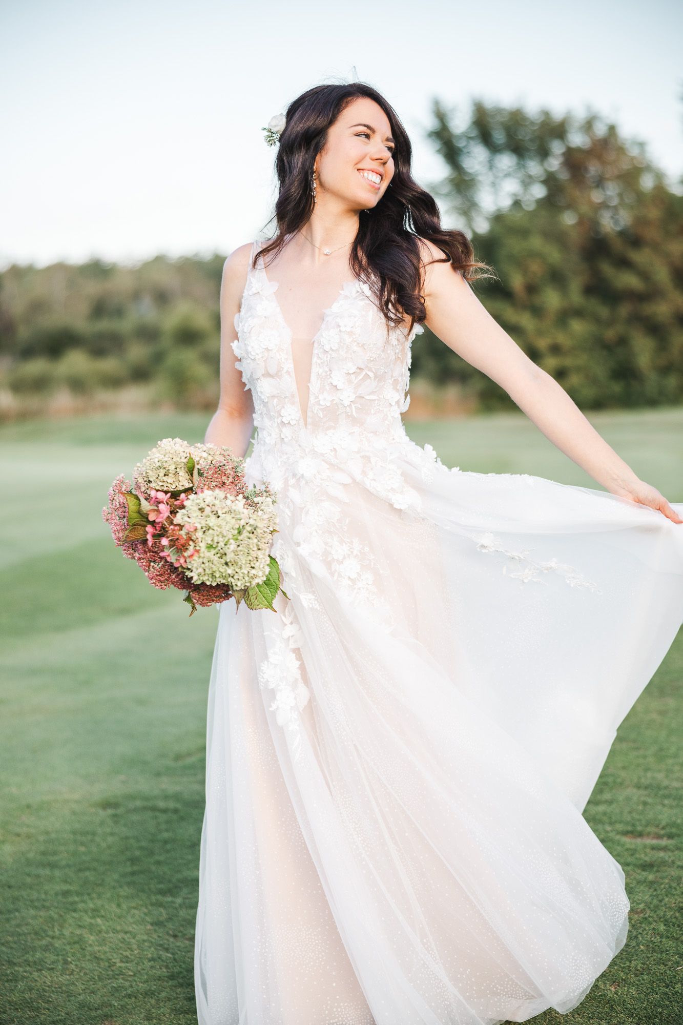 Mariée éthérée en robe blanche fluide en dentelle tournoyant joyeusement sur une pelouse, bouquet automnal à la main, en Estrie
