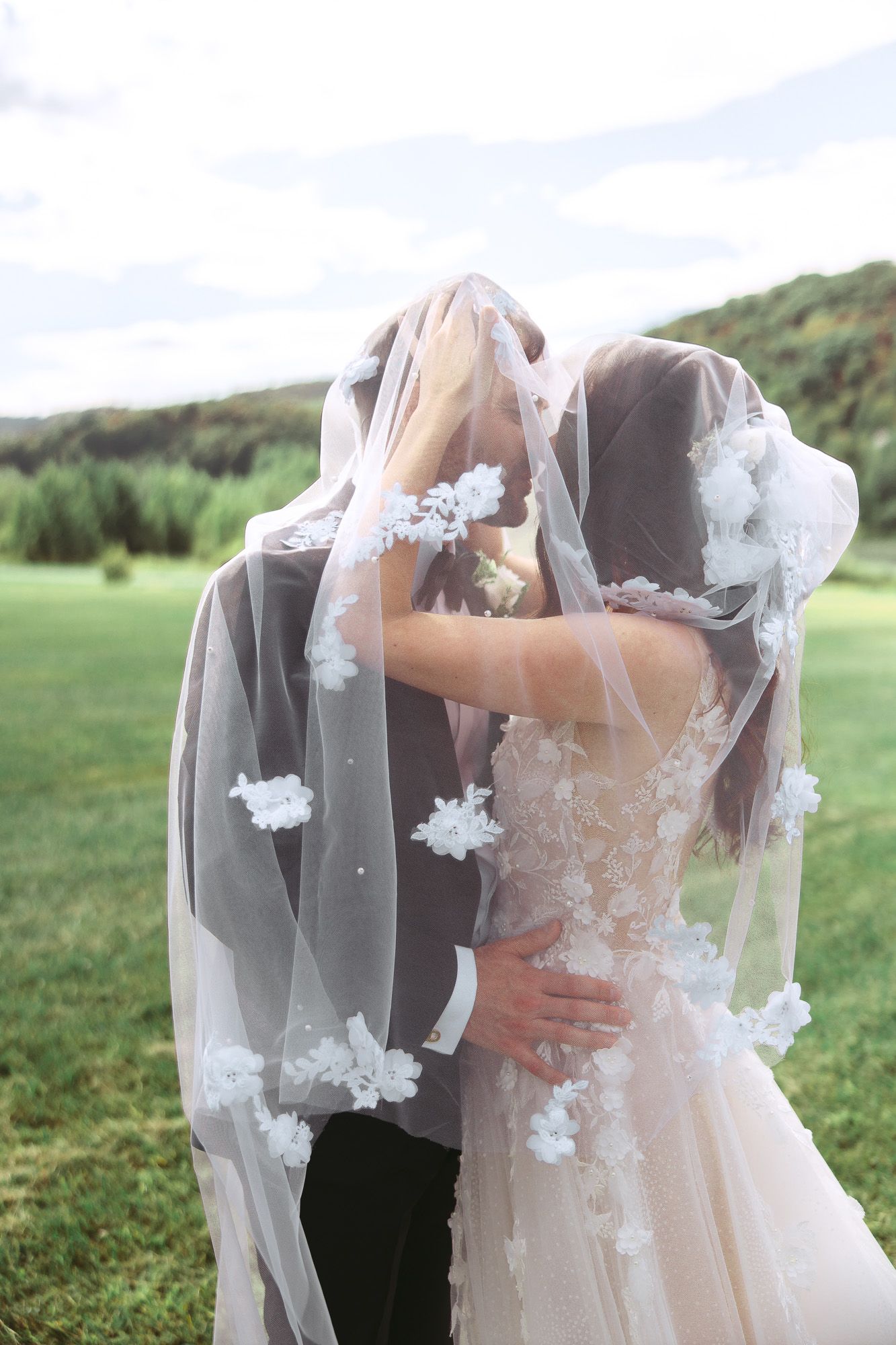 Moment romantique de mariage capté alors qu’un couple s’enlace sous un voile de dentelle délicat, dans un jardin