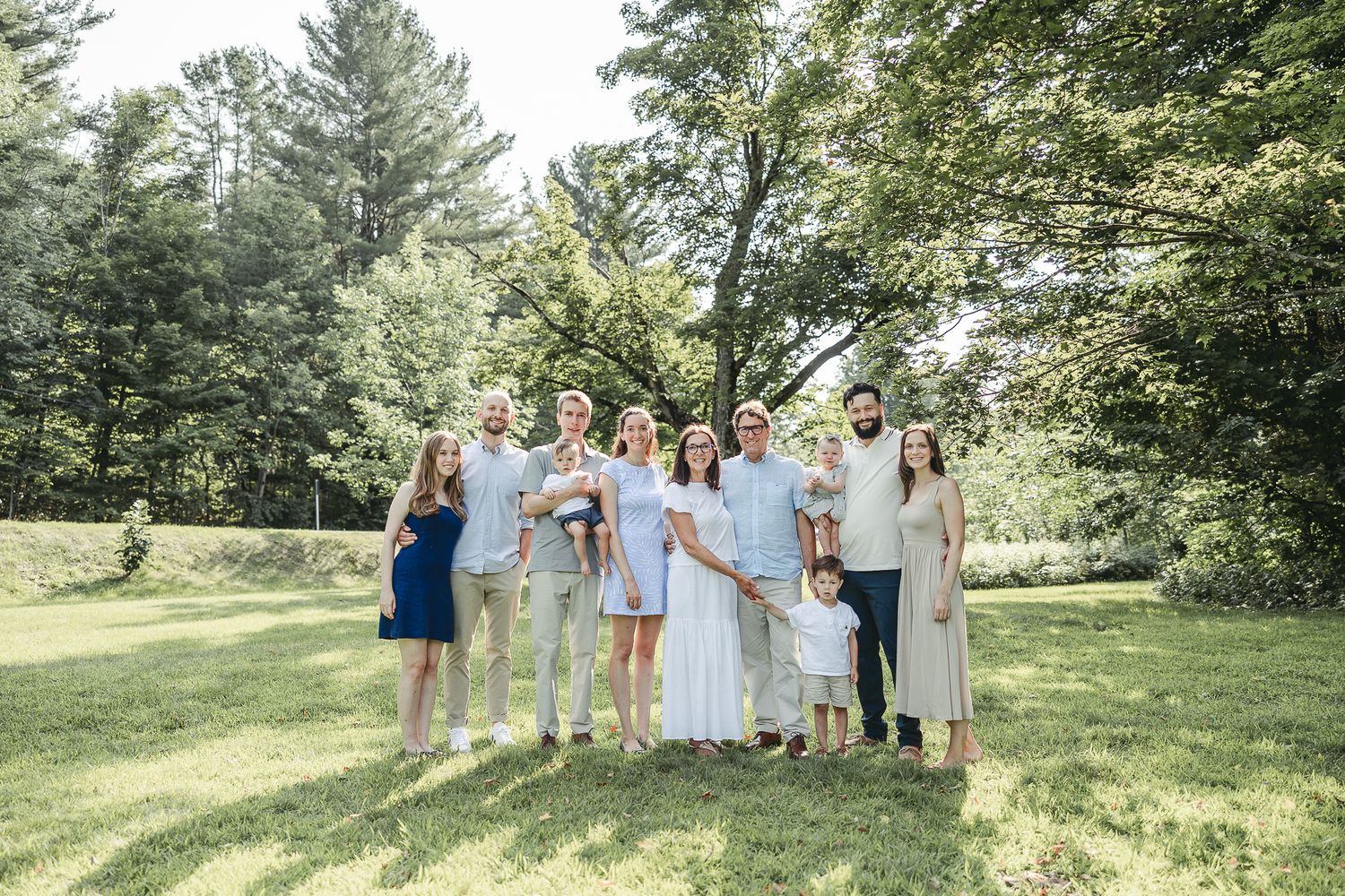 Famille intergénérationnelle en tenue formelle posant dans un parc verdoyant sous le soleil, capturée pour moments élégants et chaleureux