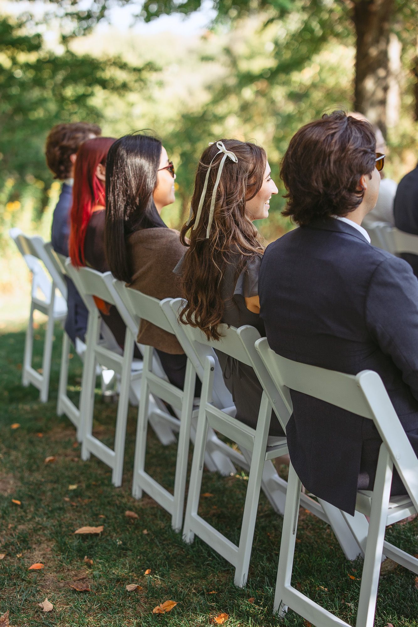 Invités de mariage assis sur des chaises blanches pliantes lors d’une cérémonie extérieure sous les arbres en automne, en Estrie