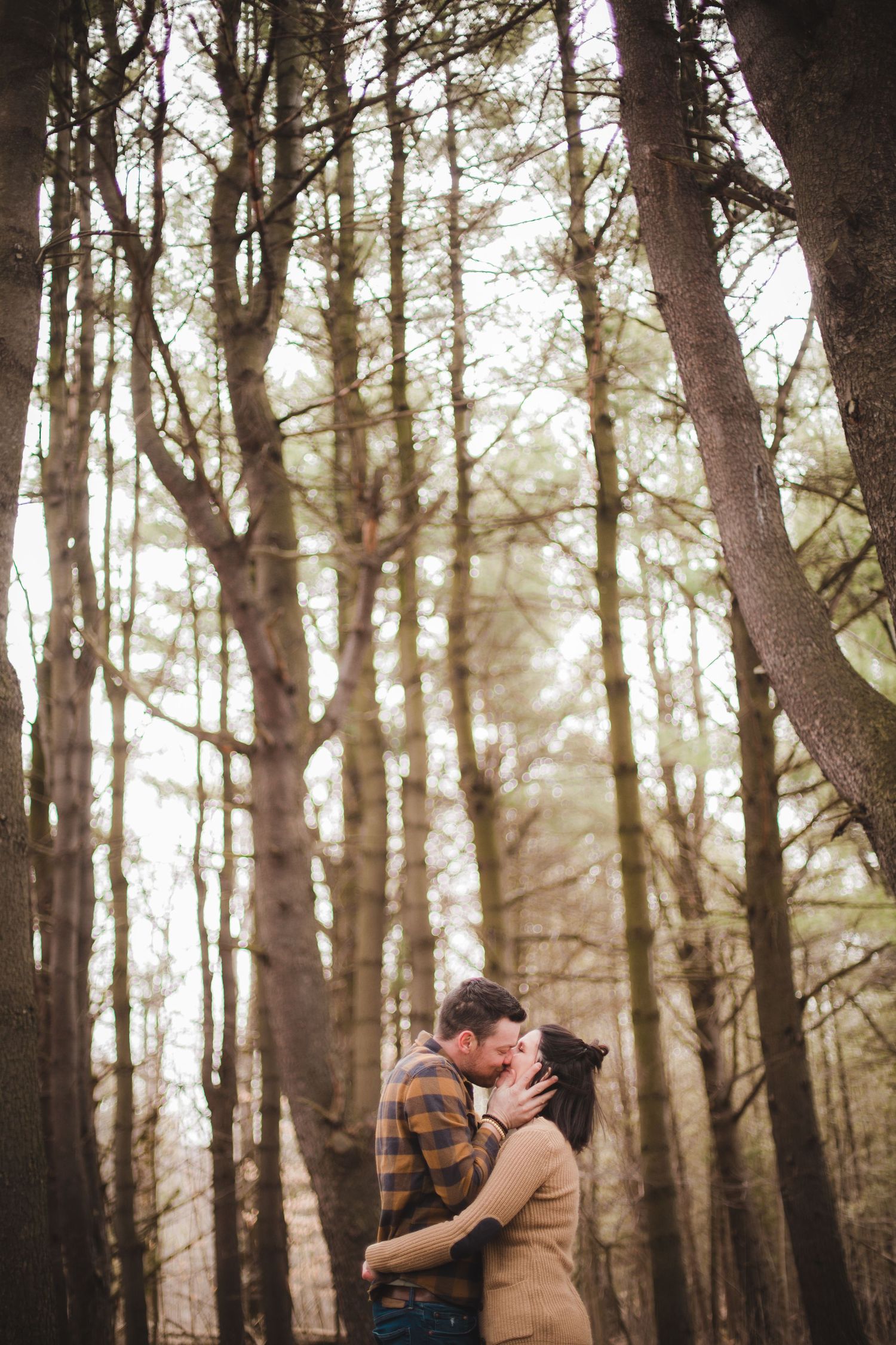 Couple capturé en étreinte romantique dans forêt brumeuse avec rayons de soleil filtrant, pour créer ambiance magique et moments intimes