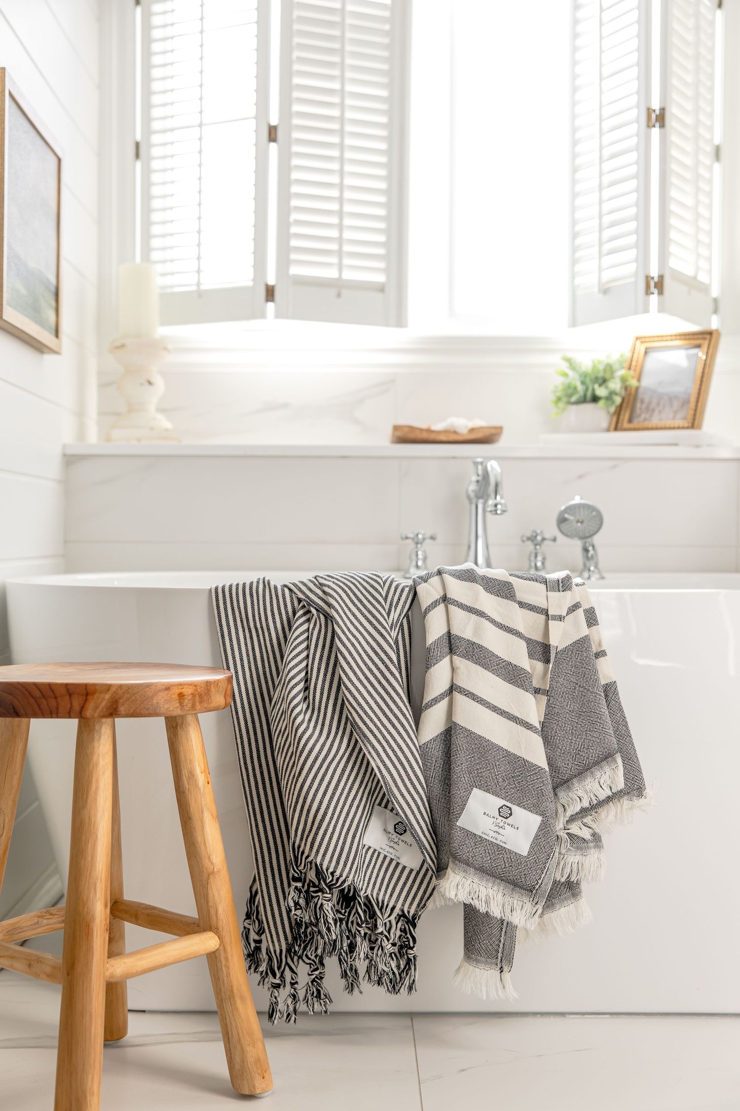 Modern bathroom interior with white tub, wooden stool, and striped gray Turkish towels draped over bathtub edge.