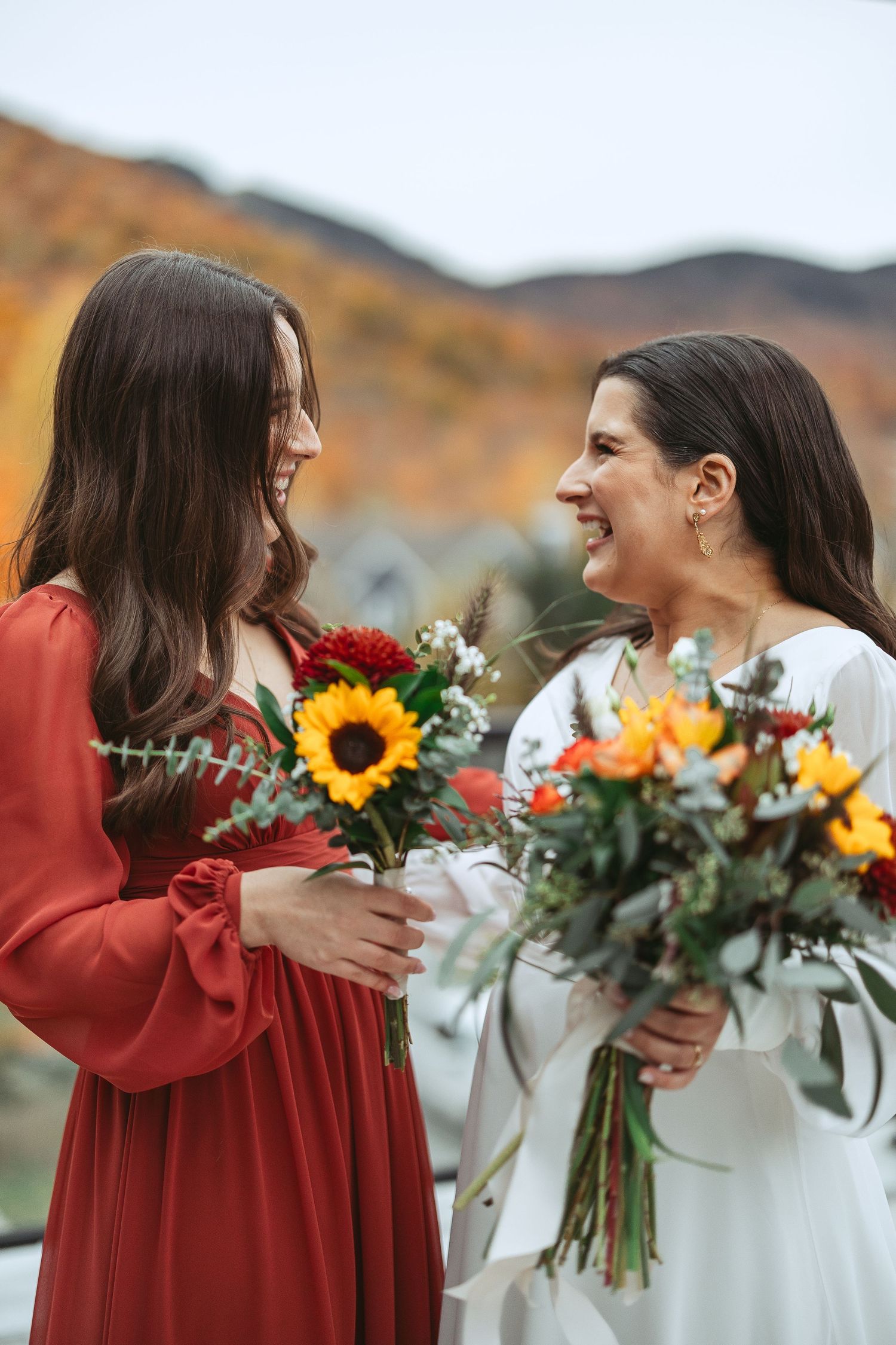 Two people in red and white outfits share a joyful moment while holding beautiful autumn bouquets with sunflowers.