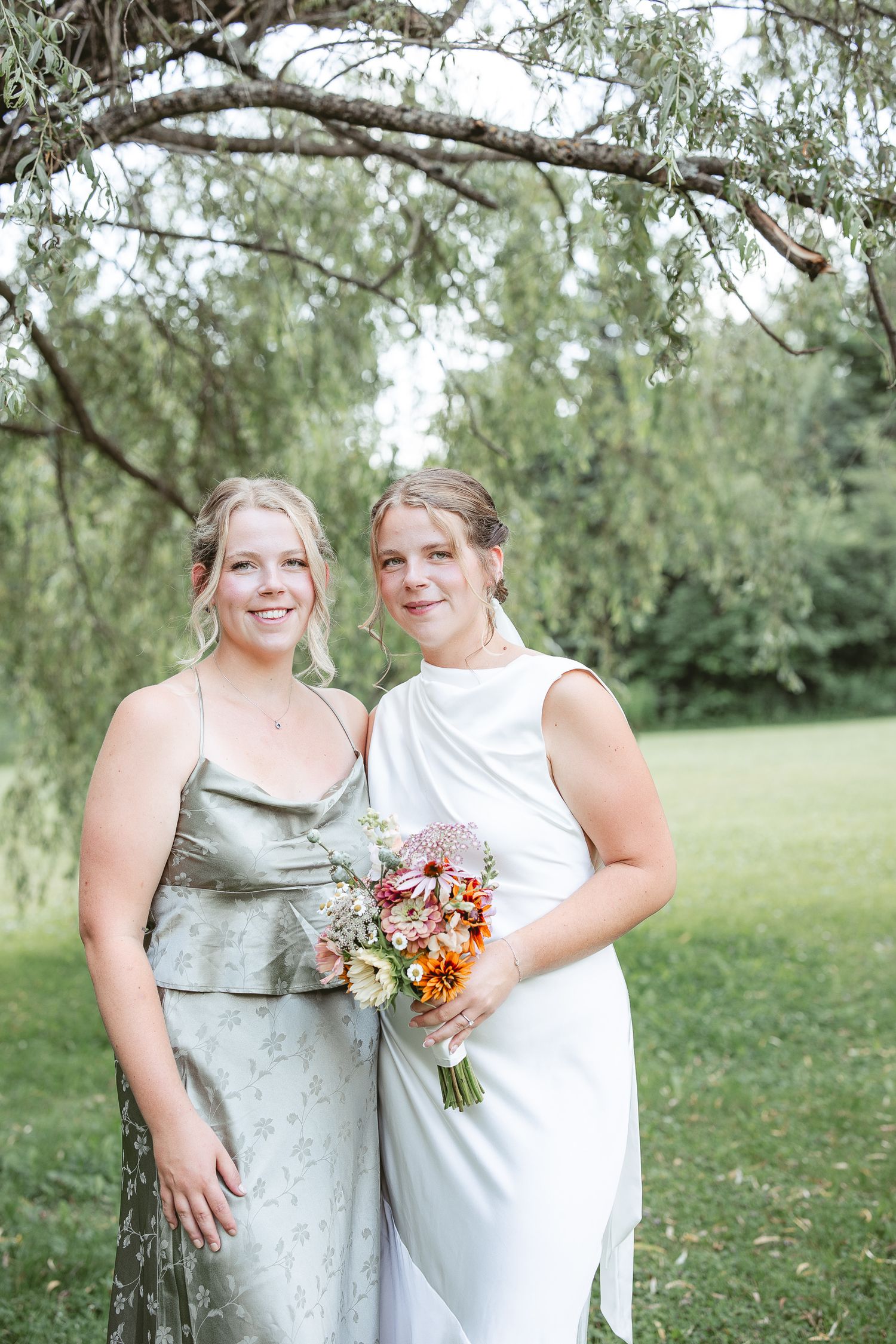 la mariée et sa soeur posant en extérieur sous des saules, tenant un bouquet floral coloré