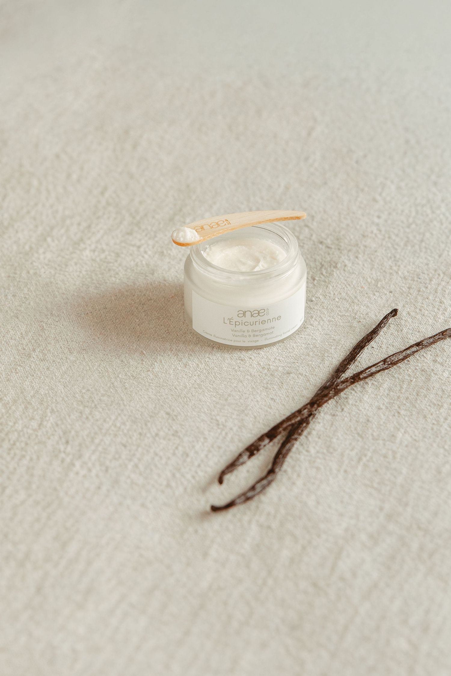 White skincare cream jar with wooden spoon on light linen fabric.