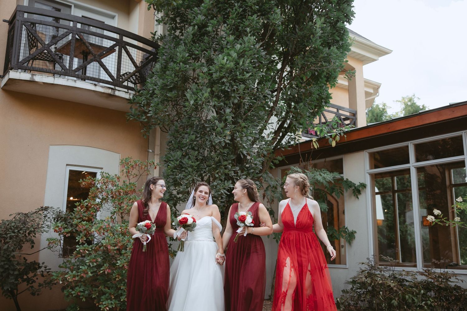 Wedding party in burgundy and white dresses gathered outside venue building.
