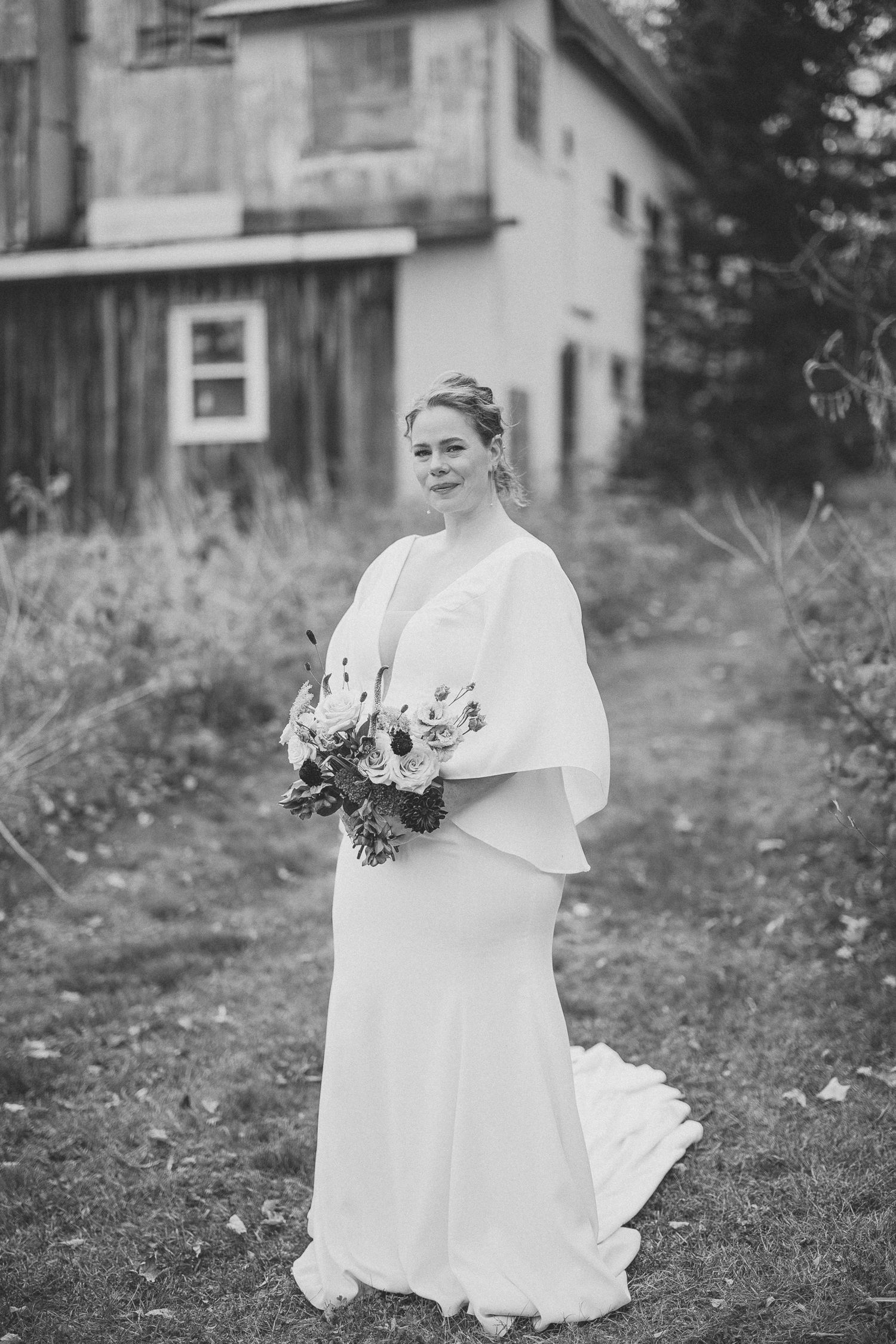 Portrait noir et blanc de la mariée avec son bouquet avec une ferme rustique en arrière plan