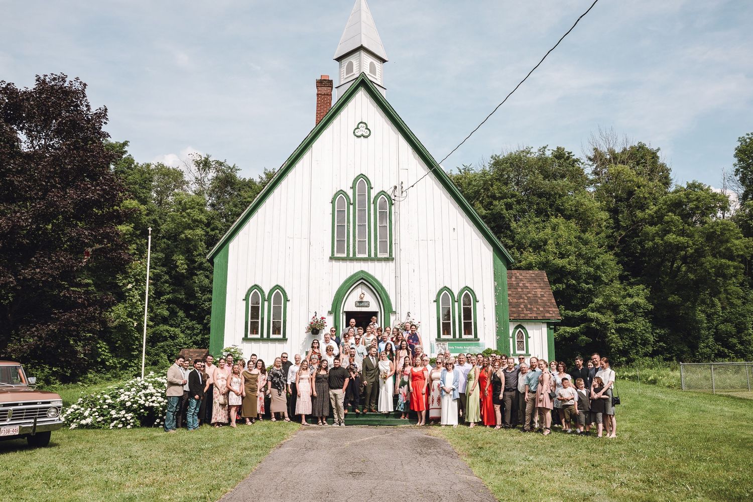 Invités rassemblés devant une chapelle blanche champêtre lors d’une célébration de mariage pour la photo de groupe