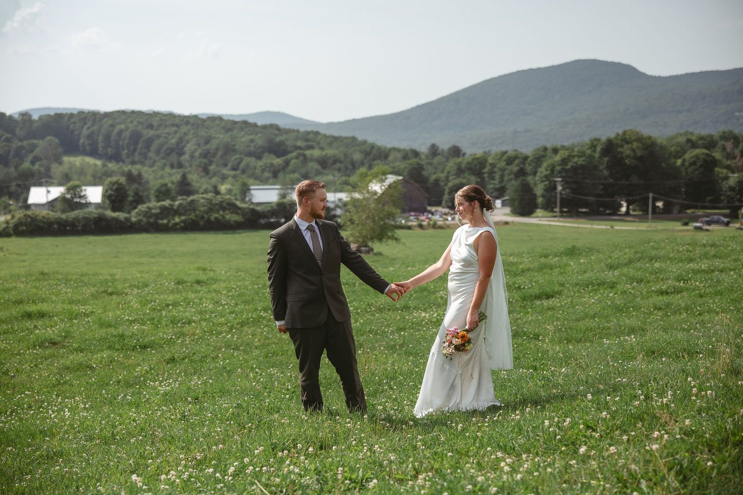 Couple se tenant la main dans un pré verdoyant avec montagnes et paysage champêtre en arrière-plan