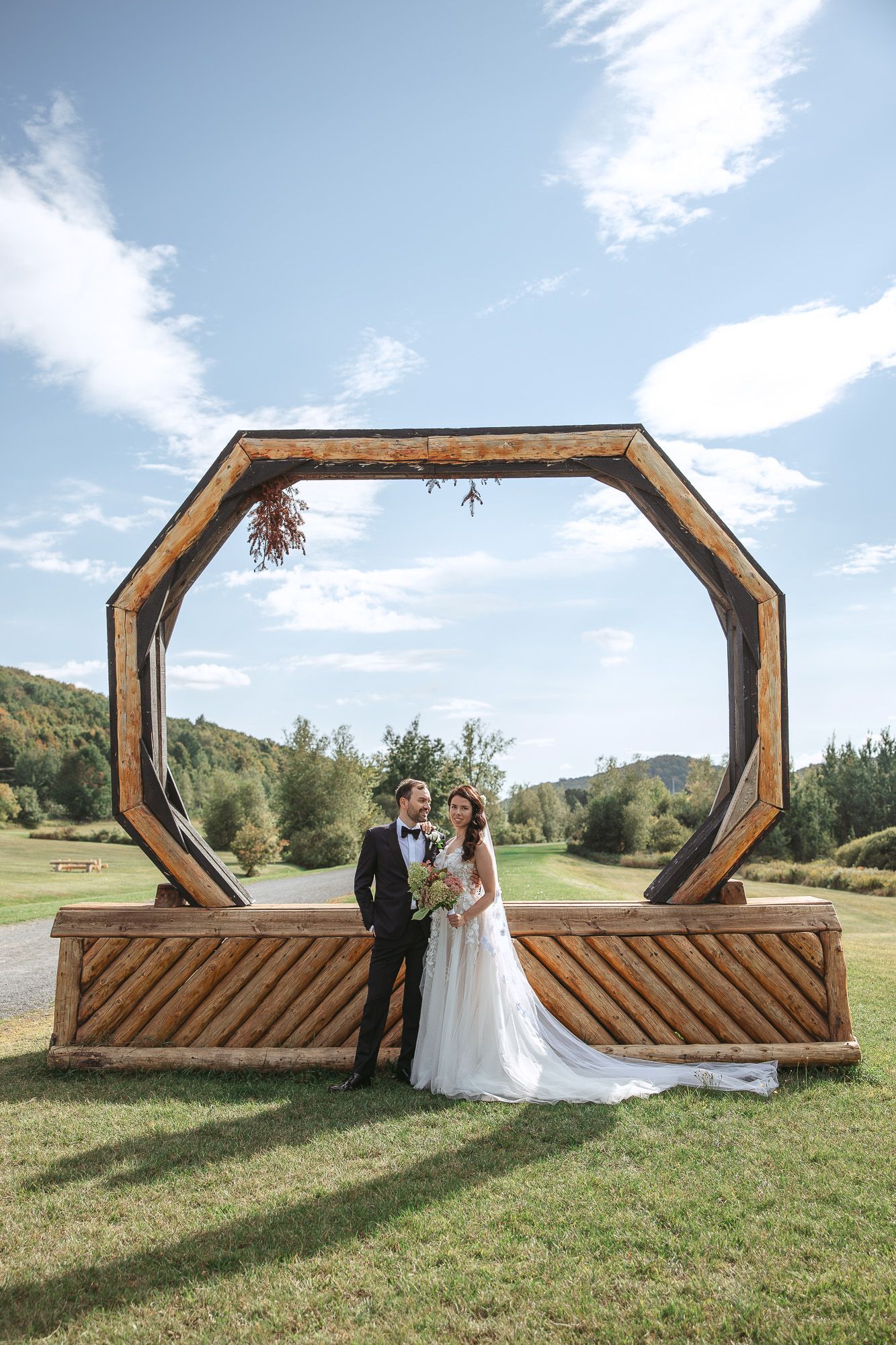 Installation de cérémonie de mariage avec arche octogonale en bois dans une prairie de montagne, en Estrie