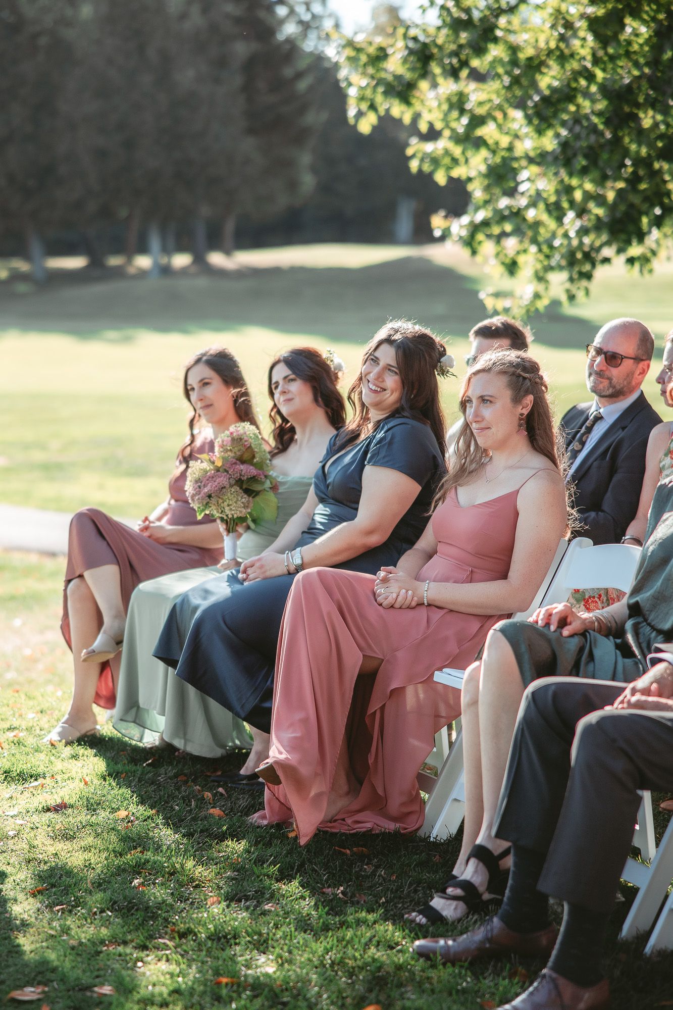 Invités de mariage riant ensemble assis en extérieur lors d’une cérémonie ensoleillée, en Estrie