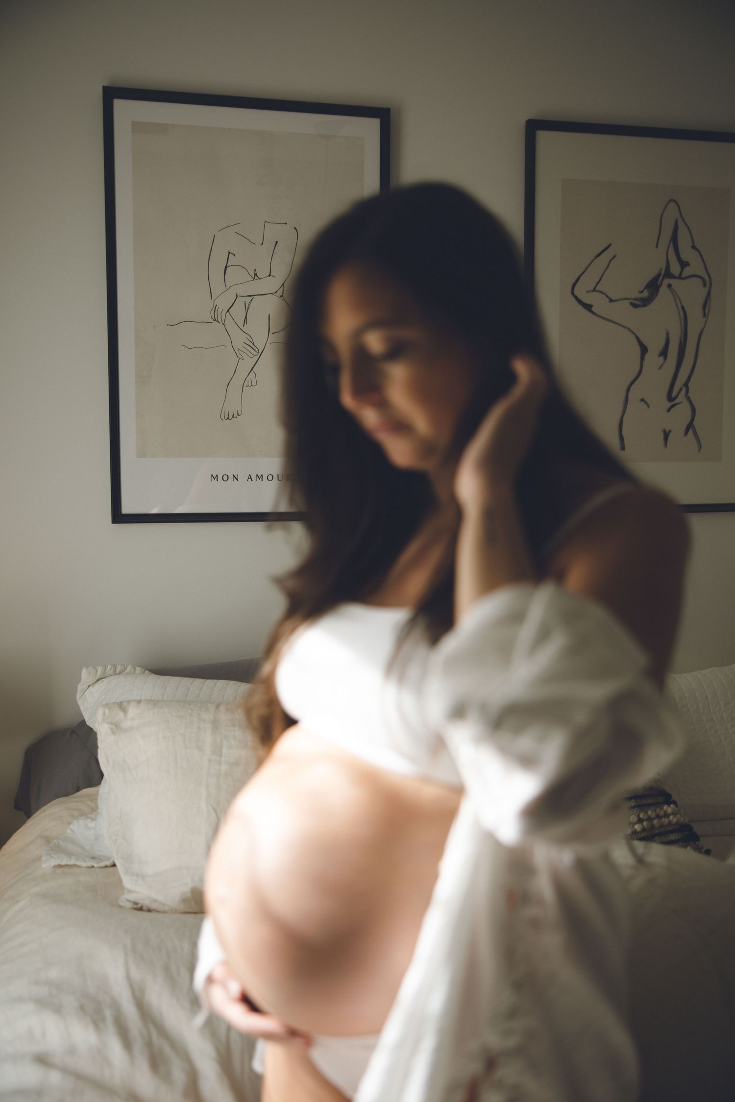 Série boudoir artistique d’une femme enceinte, lumière naturelle douce de la fenêtre et mise au point subtile pour valoriser maternité