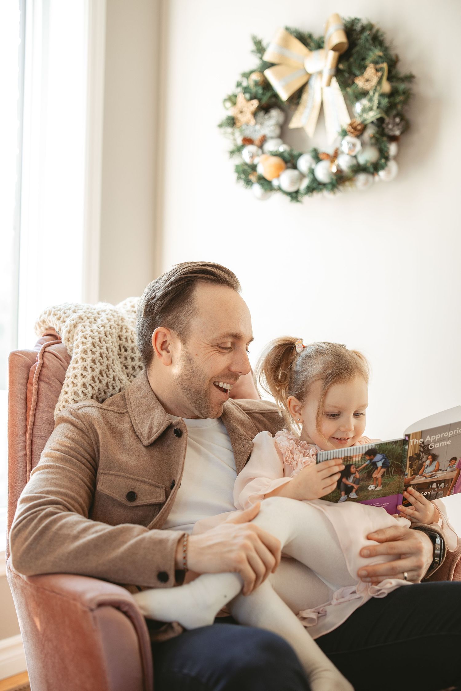 A heartwarming scene of parent and child reading a book together on a couch with holiday wreaths on the wall.