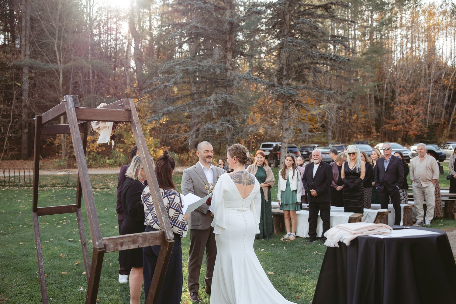 Cérémonie de mariage en plein air au cœur d’une forêt automnale, baignée d’une lumière dorée filtrant à travers les arbres.