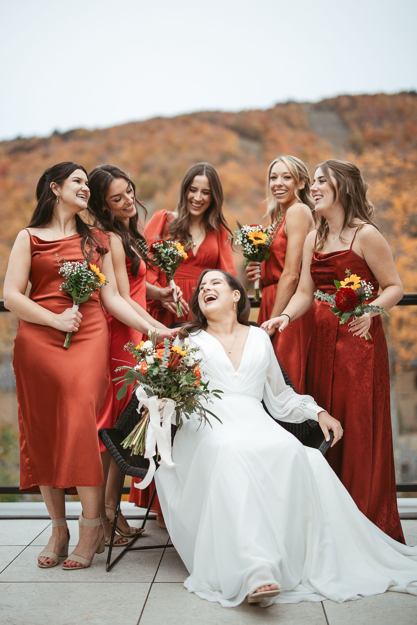Le cortège de mariage, vêtu de robes aux tons rouille et d’une robe de mariée blanche, pose ensemble lors d’une séance photo de mariage