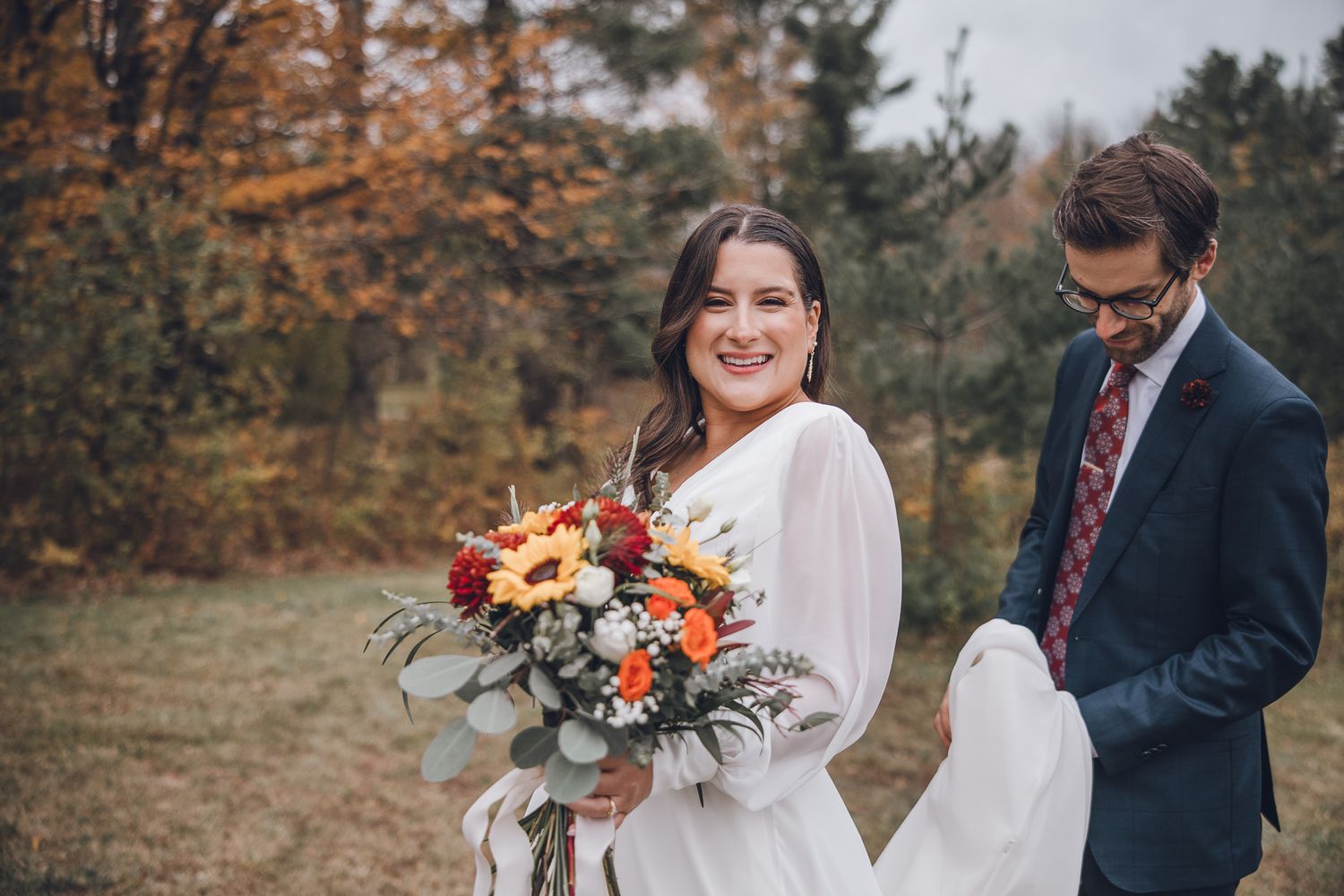 Un couple pose ensemble dans un décor forestier automnal lors de leur célébration de mariage, entouré d’un feuillage aux couleurs vibrantes