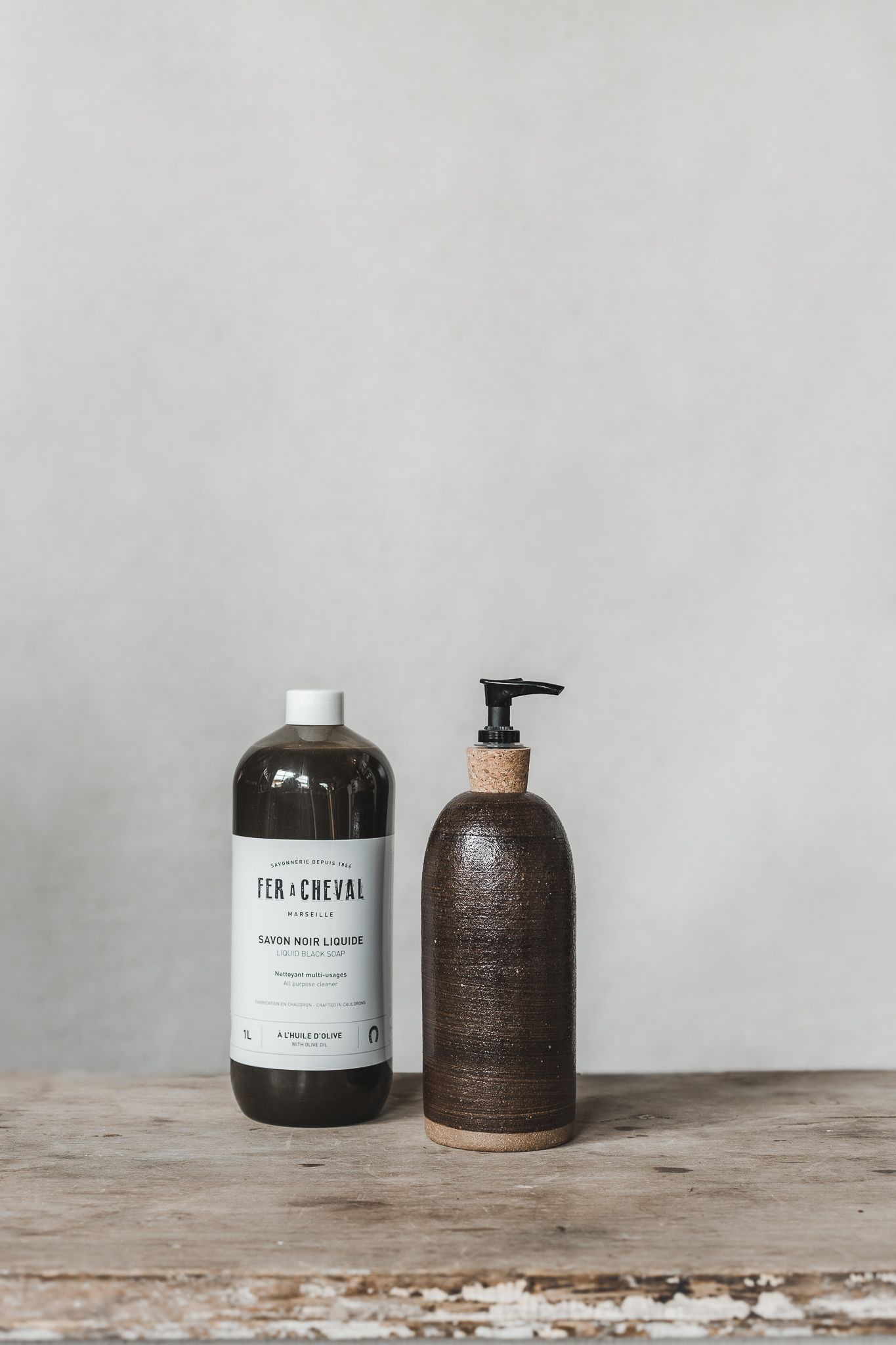 rrangement minimaliste de bouteilles et pots en céramique avec distributeur de savon blanc sur surface en bois clair, fond gris, valorisatio