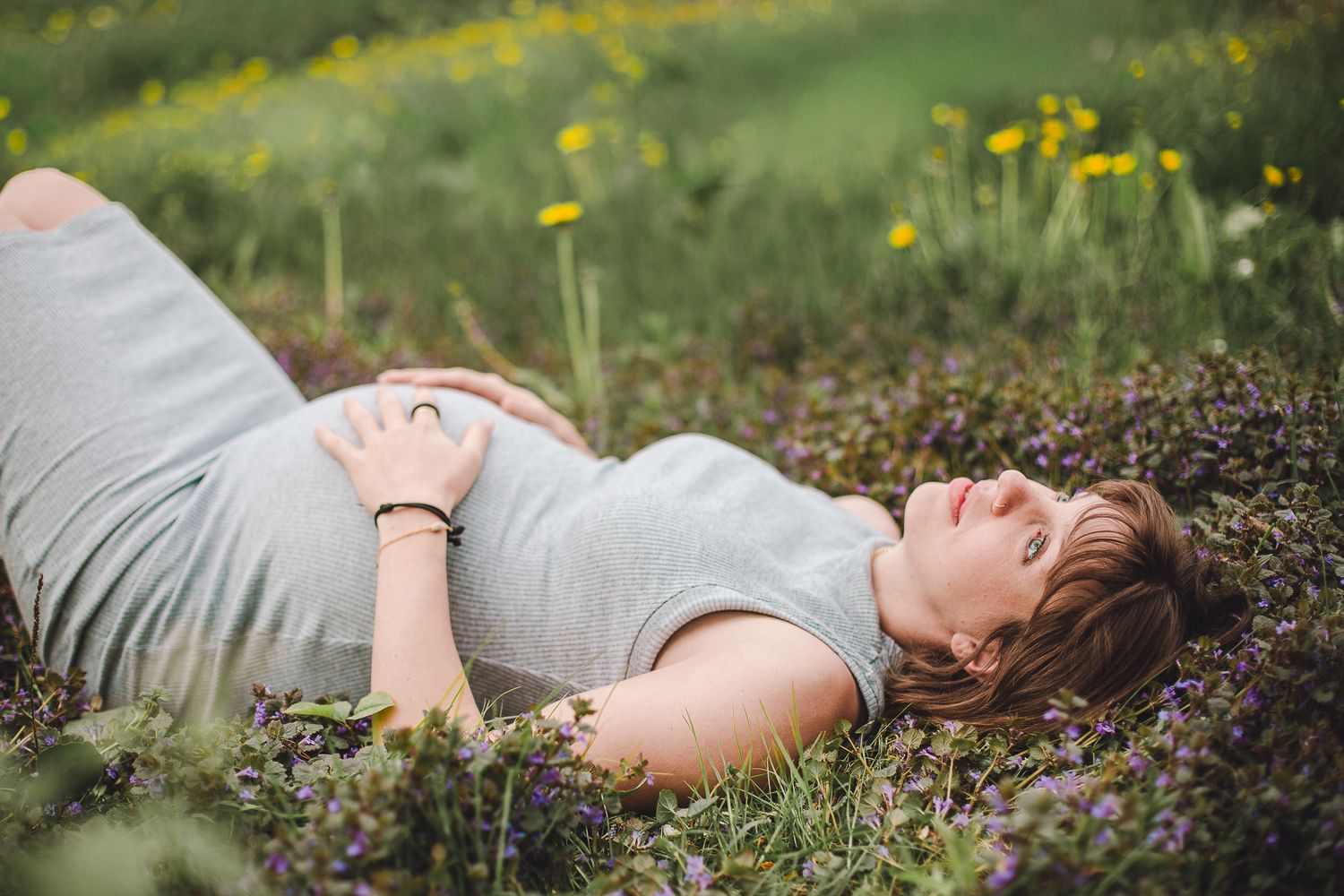 Séance maternité : femme enceinte allongée dans prairie fleurie avec fleurs jaunes et violettes, capturée pour moments doux et naturels.