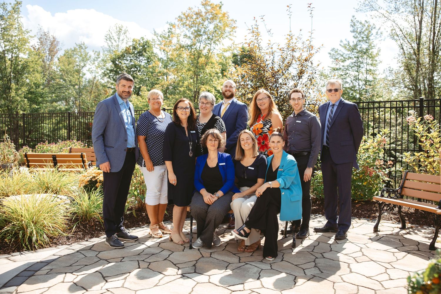 A group of people standing together outdoors on a stone patio during a sunny autumn day.
