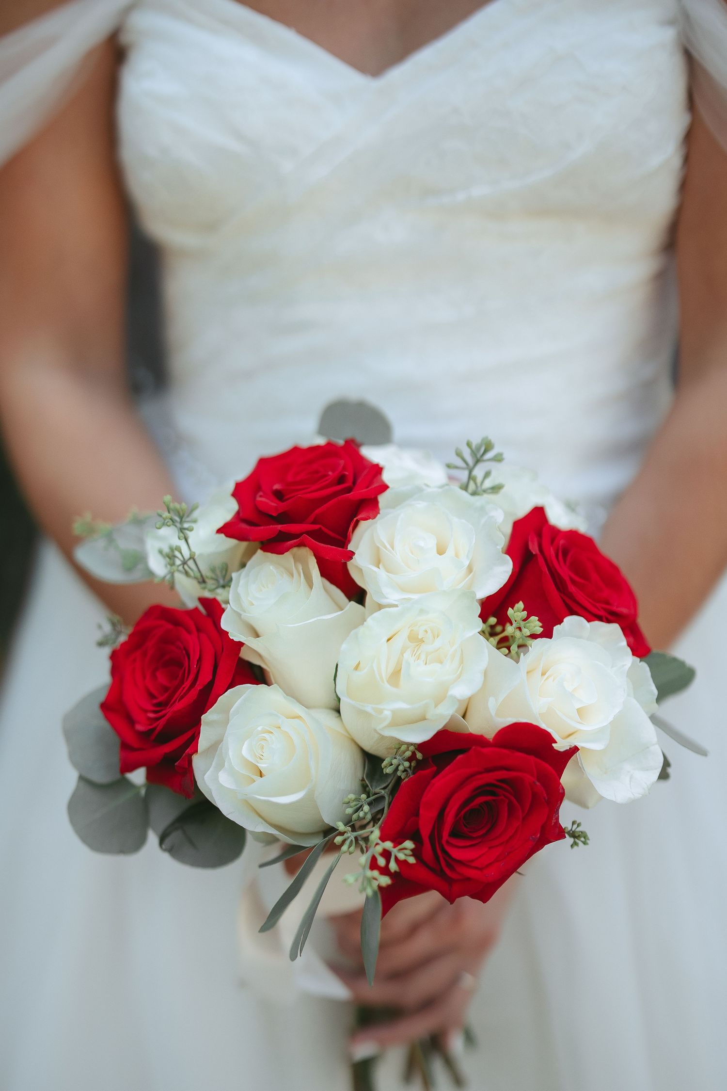 A wedding bouquet featuring a mix of red and white roses with delicate greenery against a white dress background.