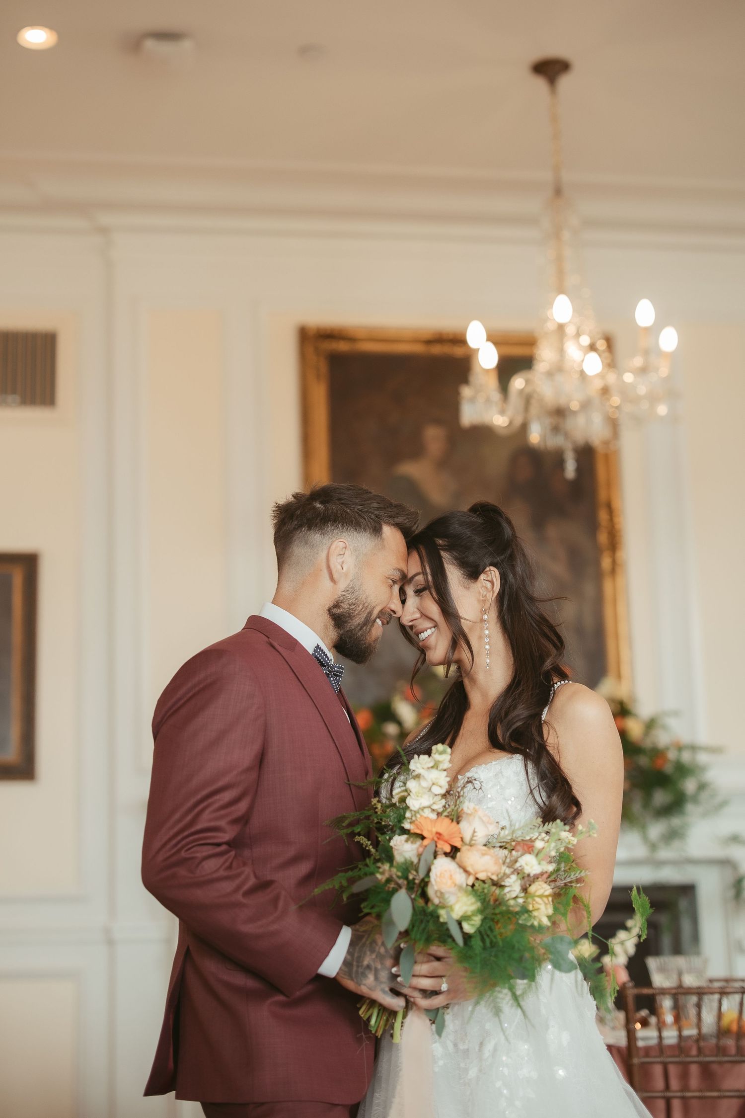 A romantic wedding moment with the bride in white lace and groom in burgundy suit sharing an intimate embrace.