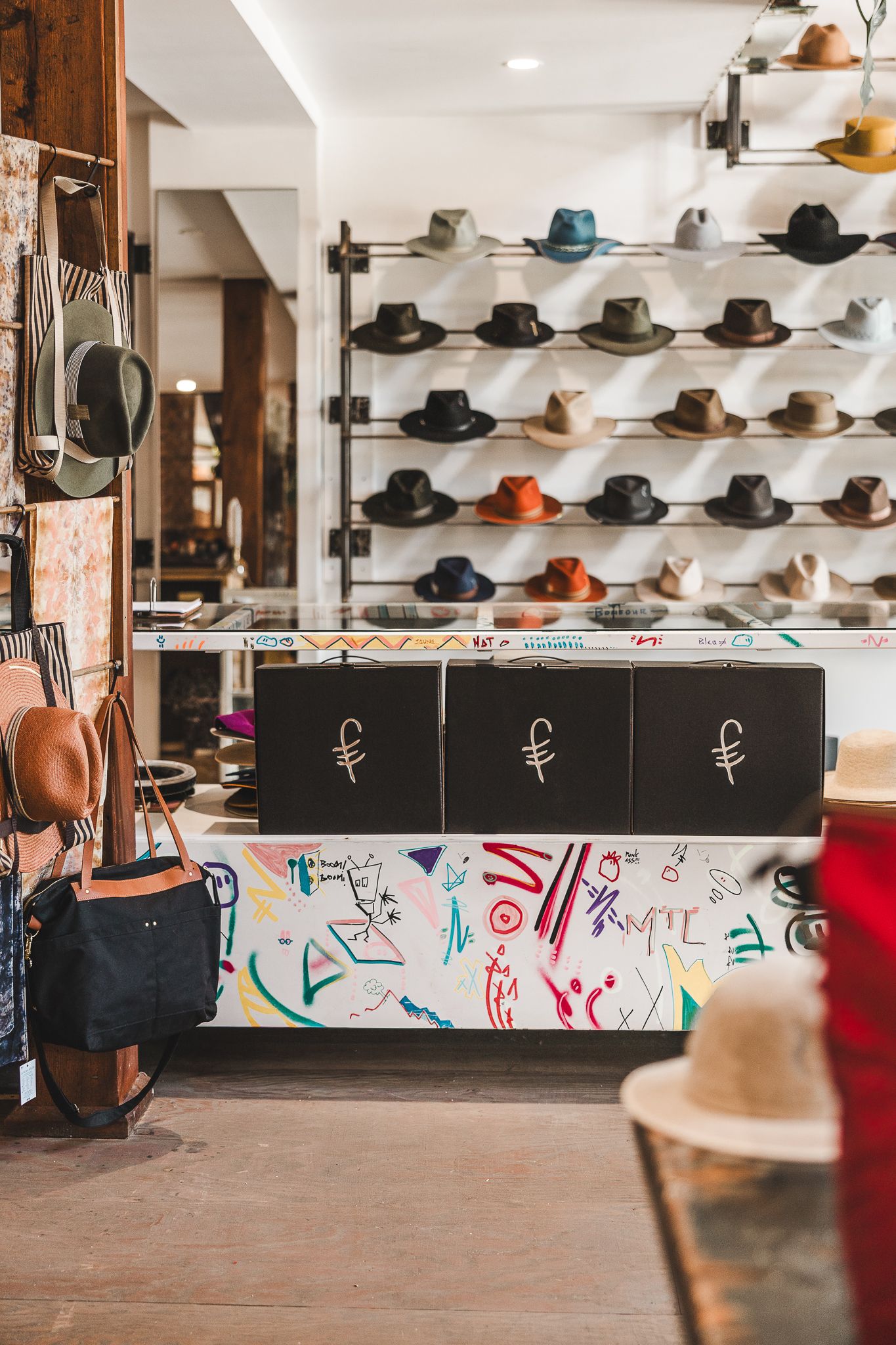 Interior view of a hat shop displaying rows of stylish fedoras and western hats mounted on wall racks above black boxes.