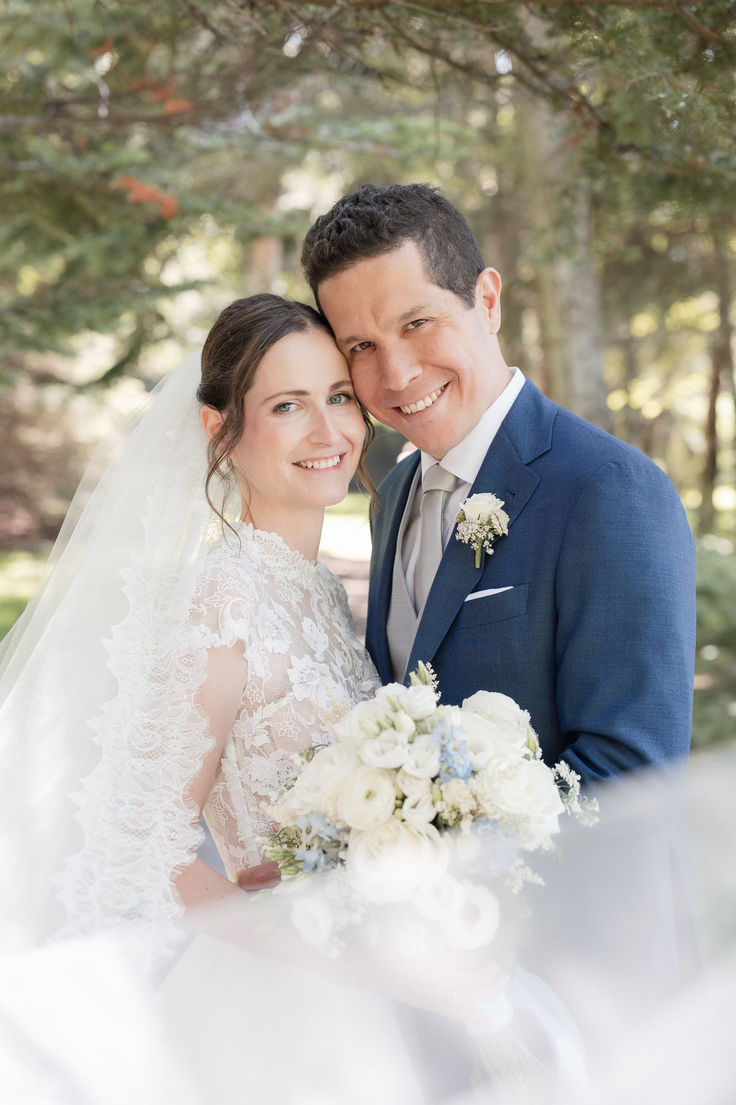 Photo de mariage montrant un couple en bleu marine et blanc s’enlaçant en extérieur, avec un bouquet floral blanc délicat.