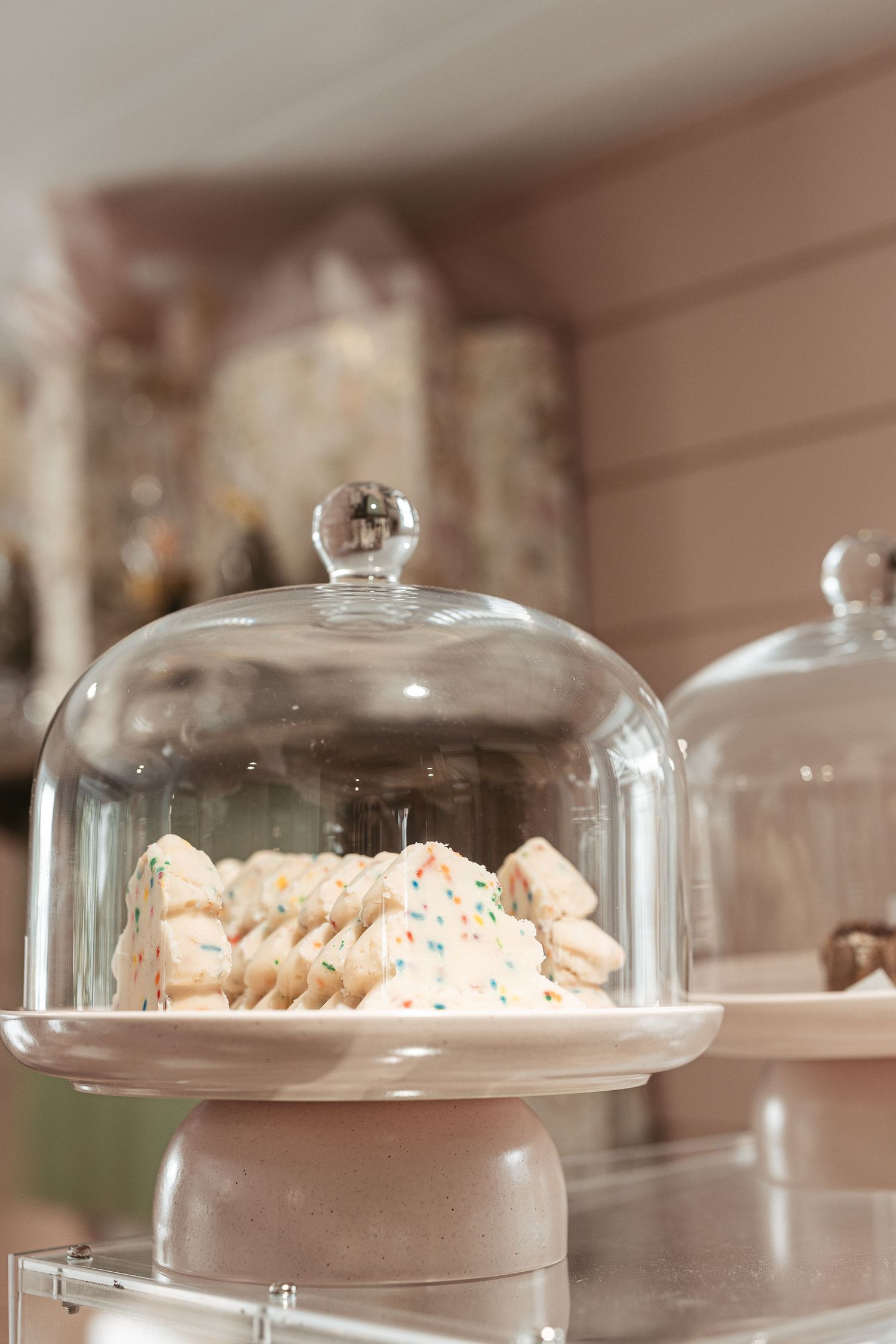 Glass cake domes displaying delicate pastries and cookies on white pedestals.