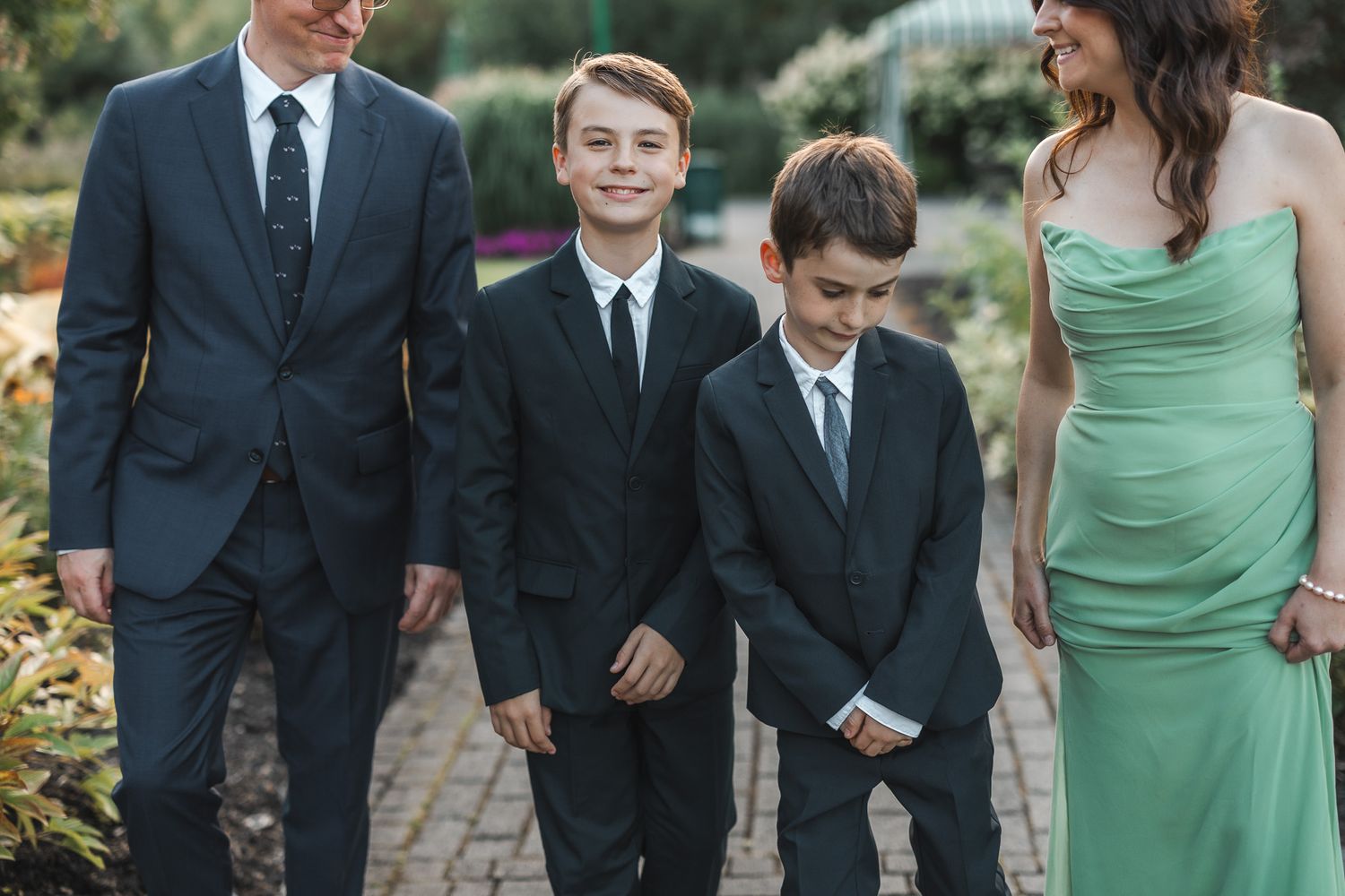 Membres du cortège de mariage réunis en extérieur, hommes en complets foncés et femmes en robes vert menthe