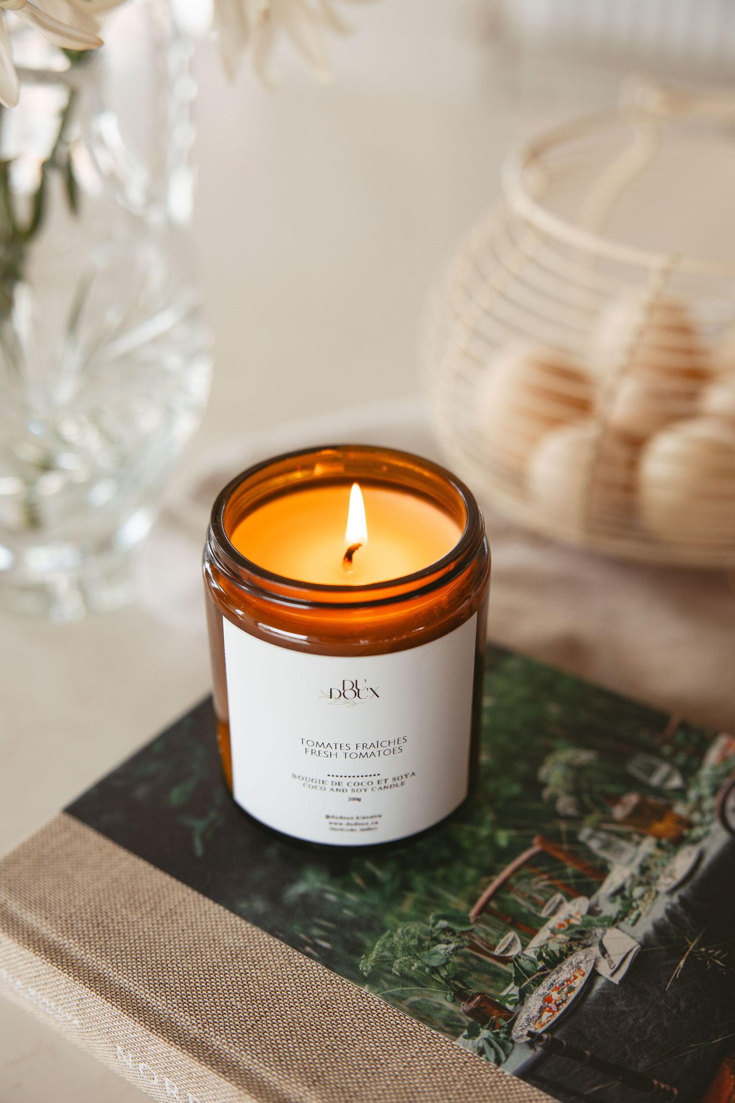 Amber glass jar candle with white label burning on stacked books, surrounded by elegant home decor accents.