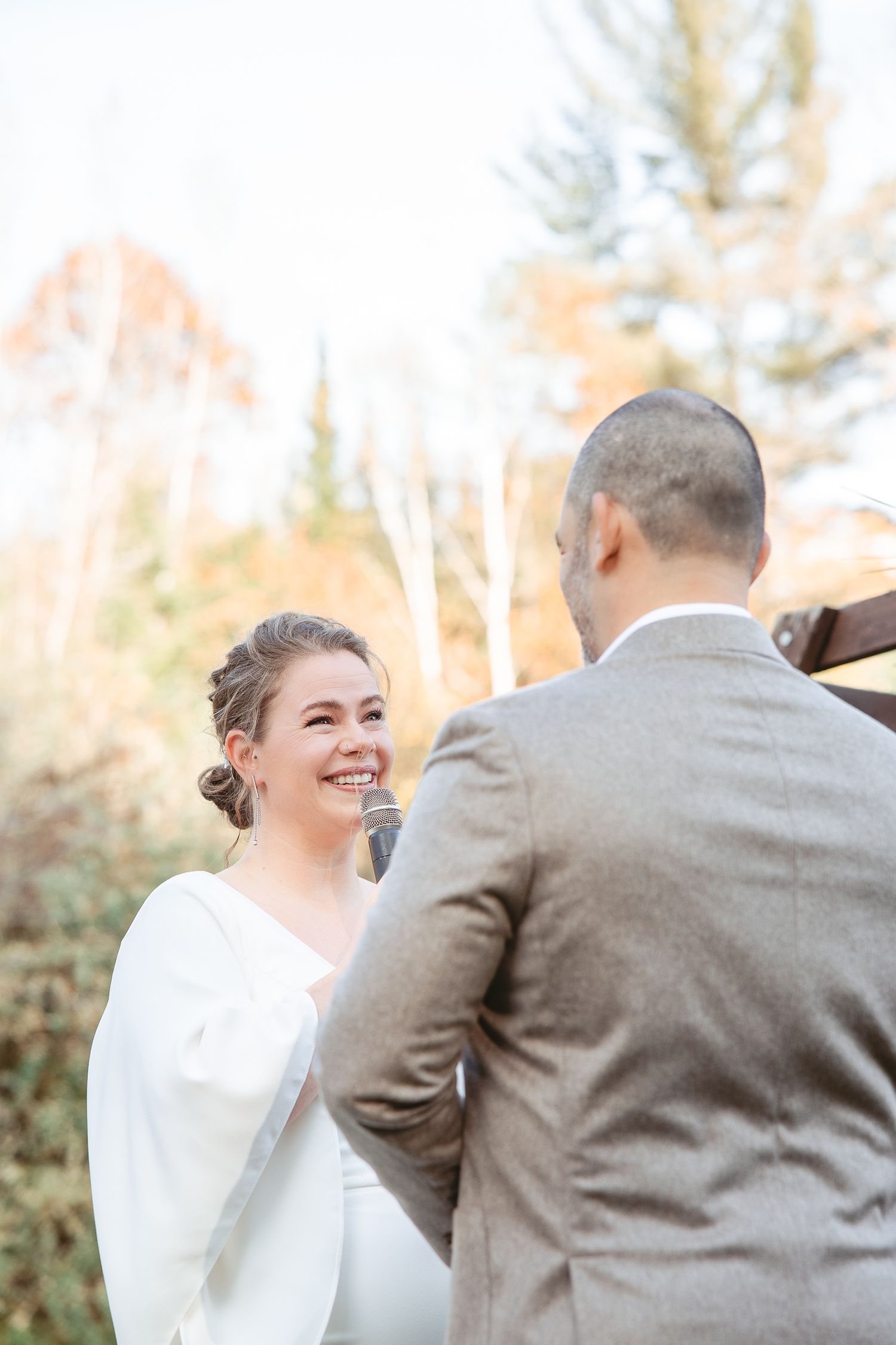 Échange de voeux lors d'un mariage en plein air au cœur d’une forêt automnale, baignée d’une lumière dorée filtrant à travers les arbres.